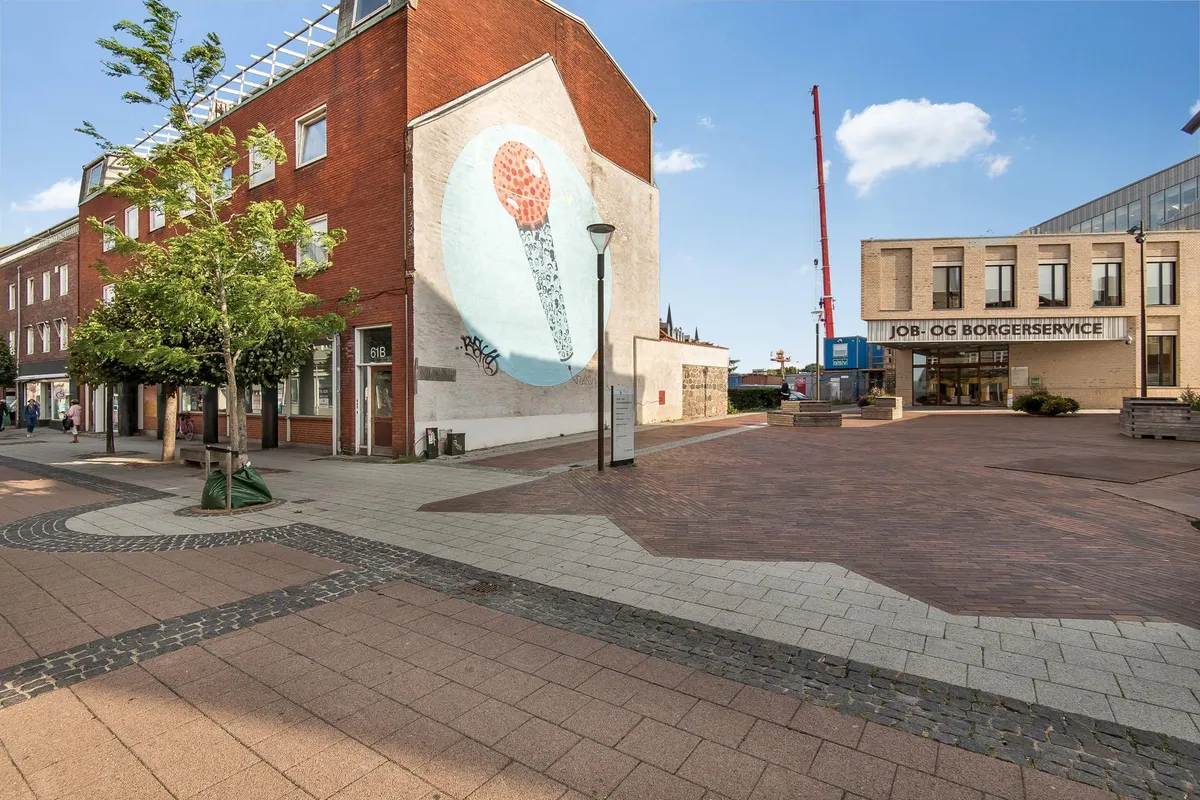 Gaden med røde mursten og et stort maleri af en mikrofon. Der er en bygning med skiltet Job og Borgerservice og en bygning