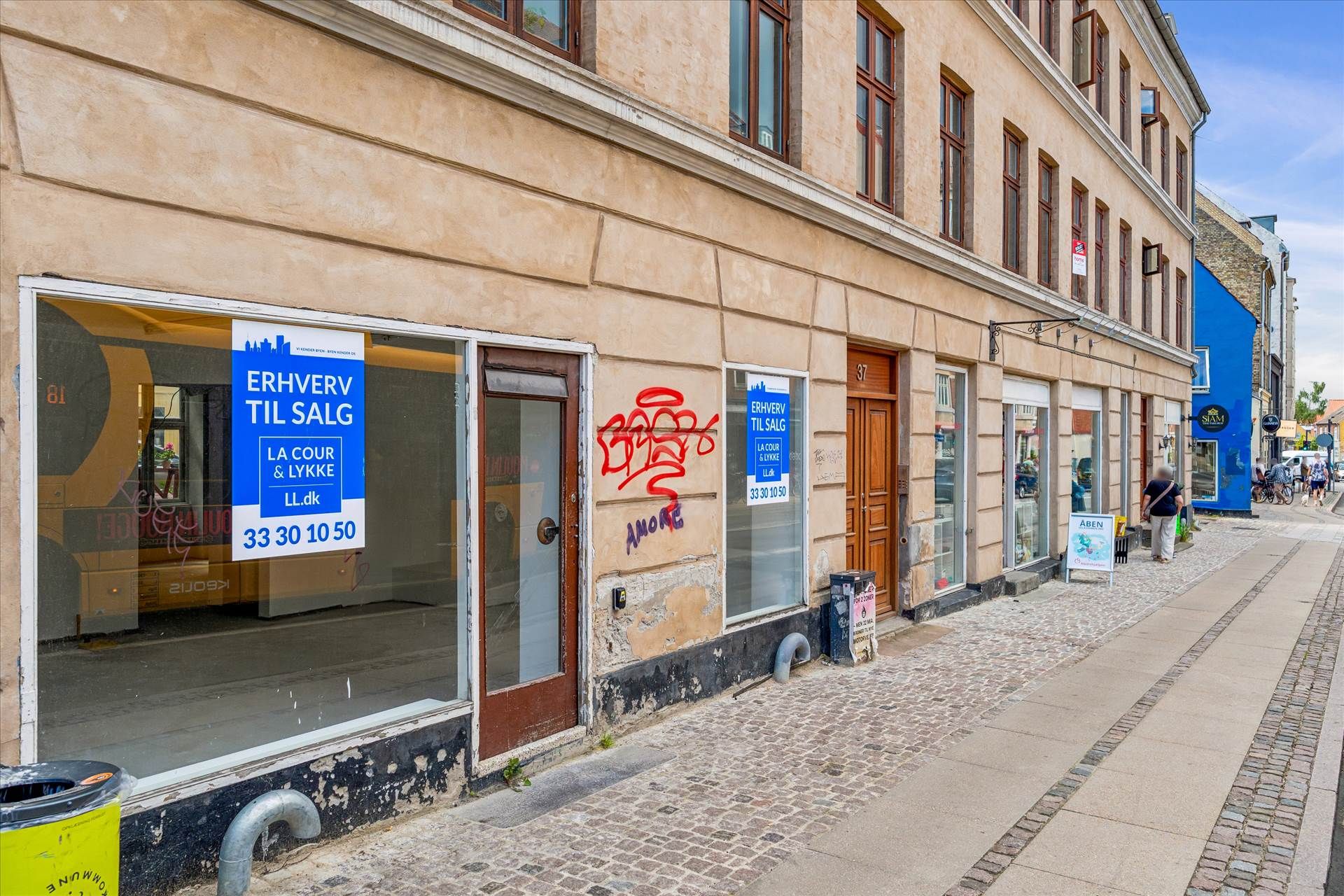 En tom erhvervsejerleilighed med salgsskilt på Valby Langgade. Skiltet viser tidligere butiksforretning og datoer. Bygning