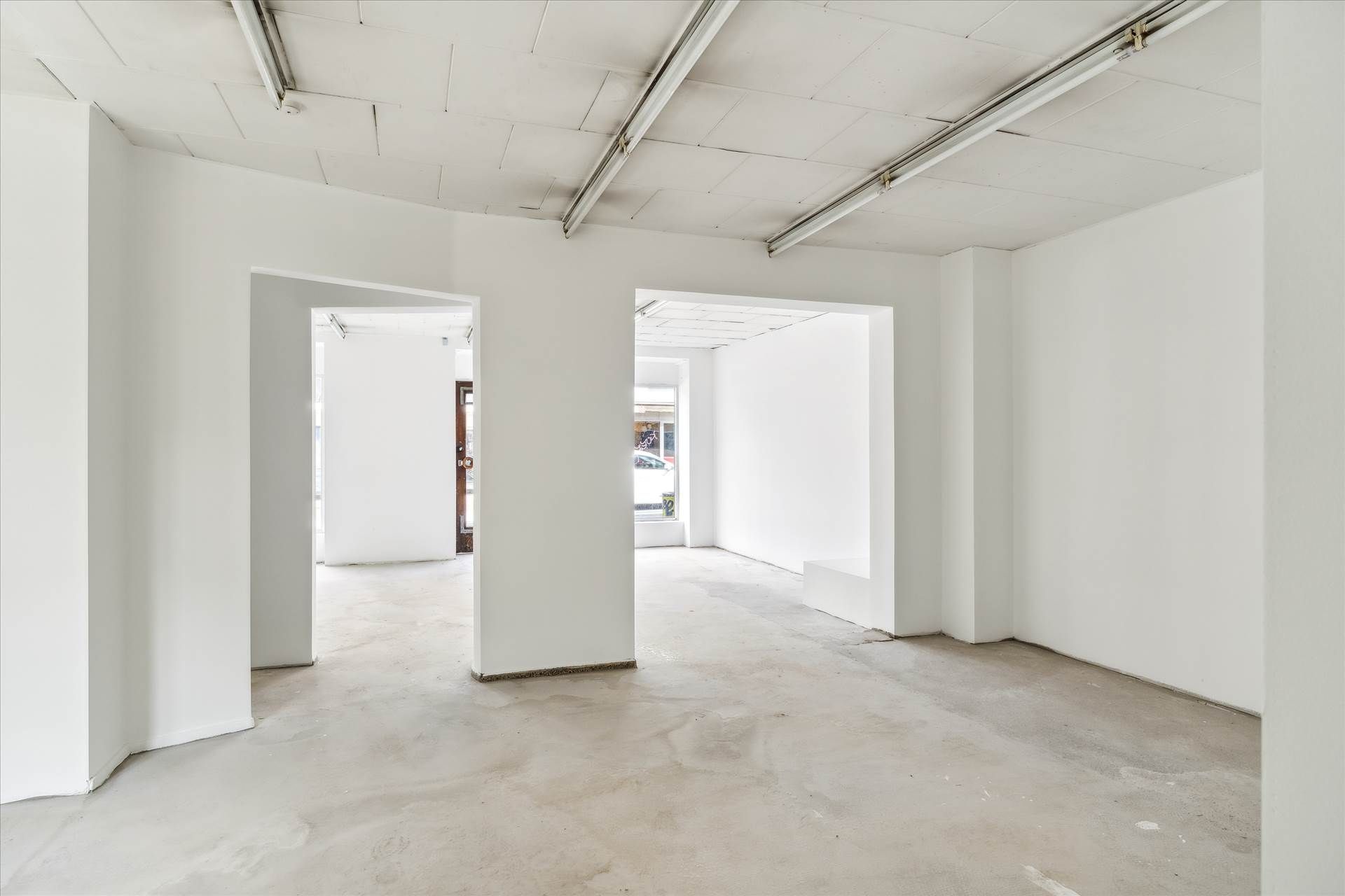 Store, hvidt lokale med lyse loftsbånd og en dør til et eksteriør med en bil og et skilt