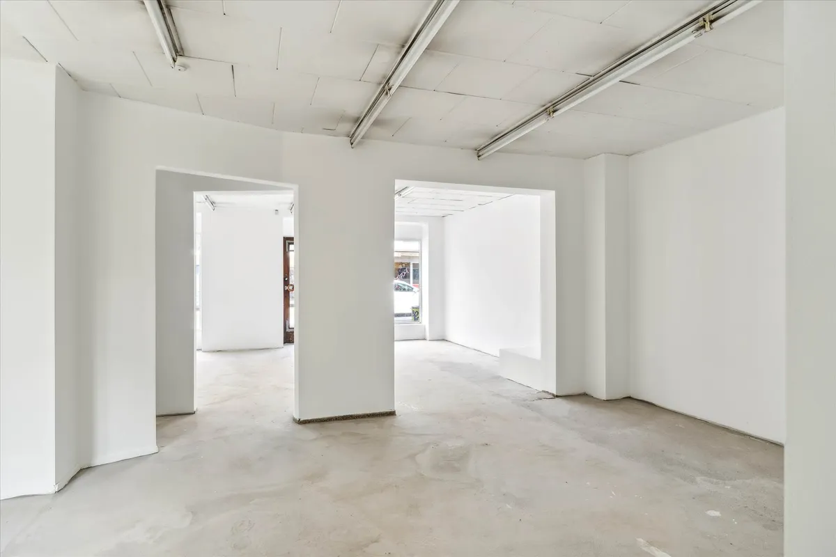 Store, hvidt lokale med lyse loftsbånd og en dør til et eksteriør med en bil og et skilt