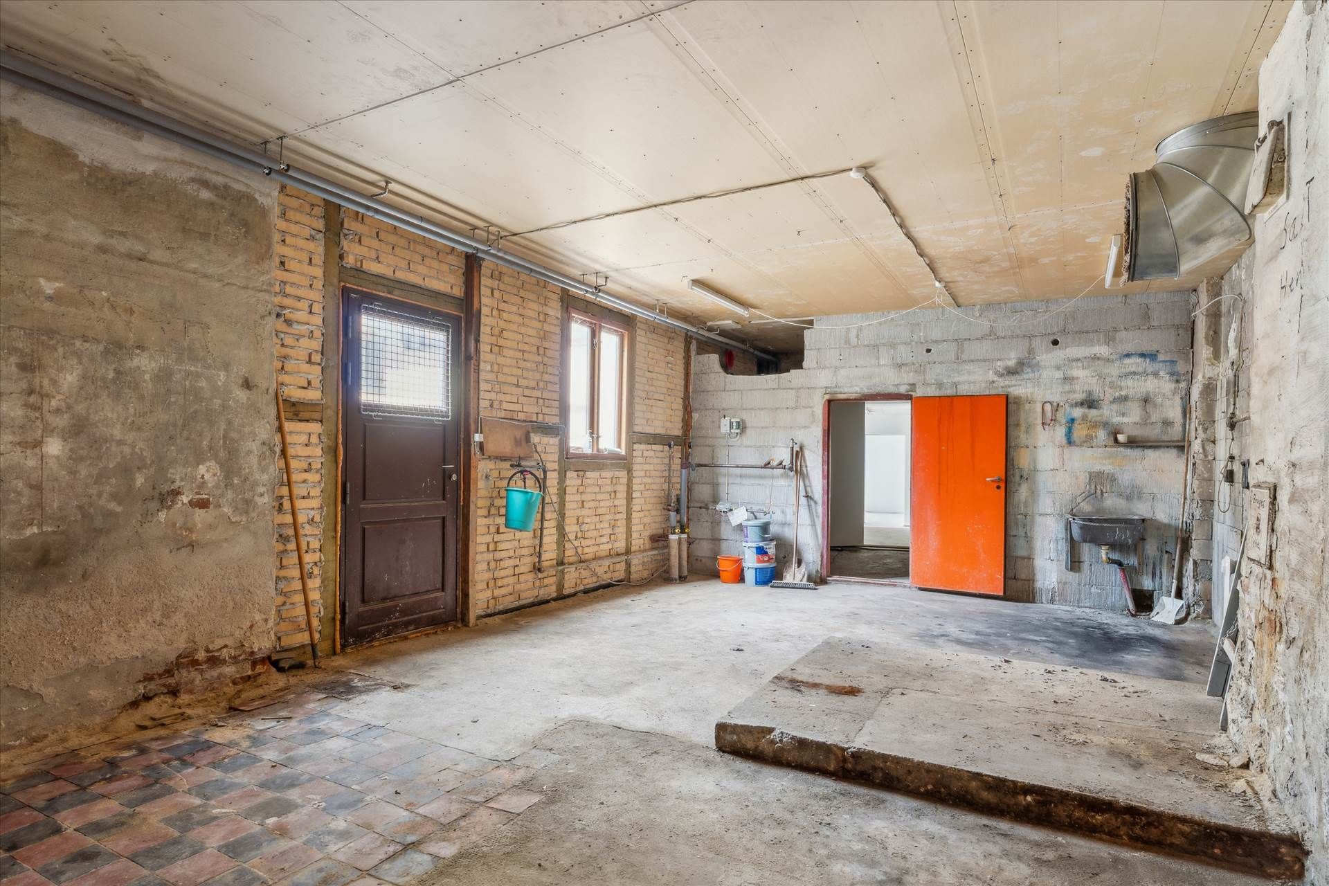 En gammel værkstedslokale med flere døre, bøjle og redskaber samt en brikmur og en gulv af beton og gulvtæppe.