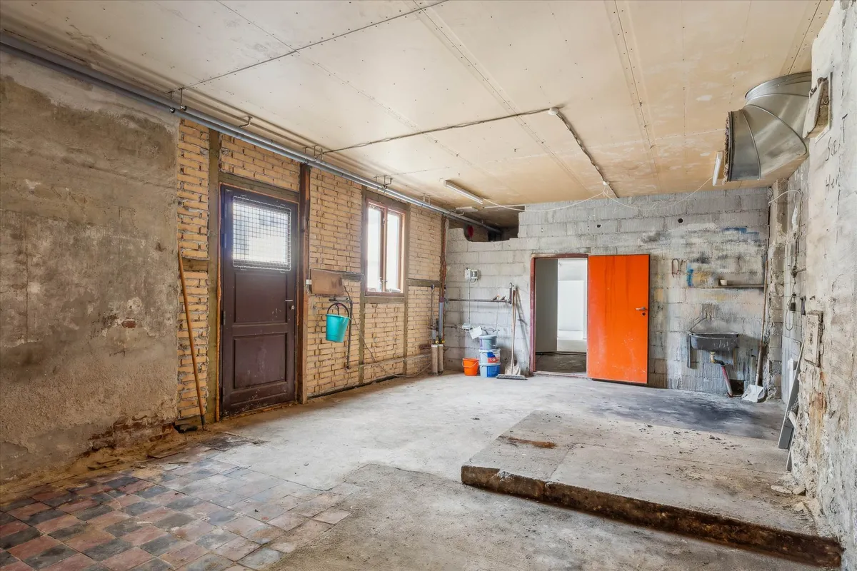 En gammel værkstedslokale med flere døre, bøjle og redskaber samt en brikmur og en gulv af beton og gulvtæppe.
