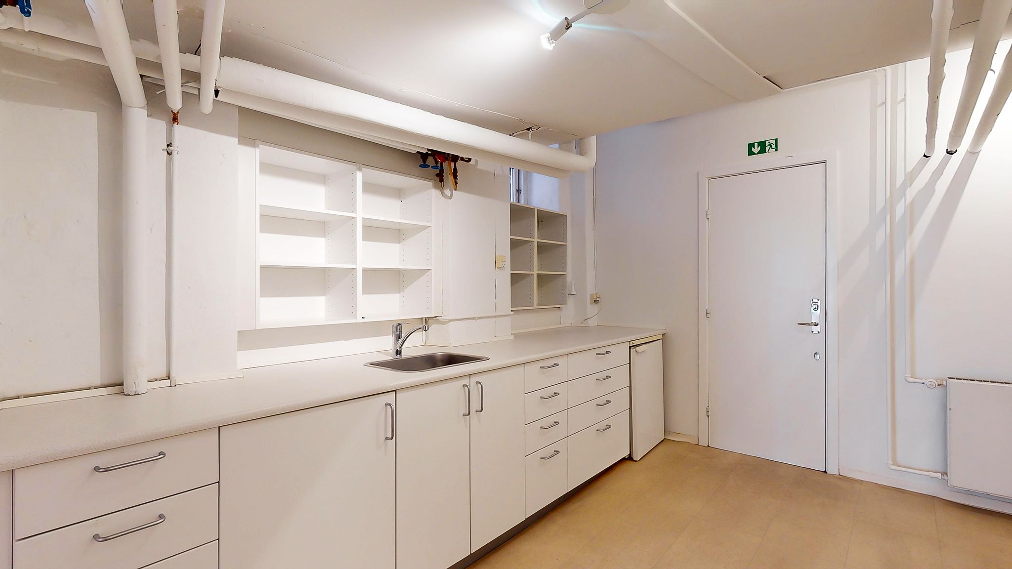 Funktionelt værelse med hvide vægge, hvide køkkenskabe og en vask med vandhane og opvaskemaskine i hjørnet