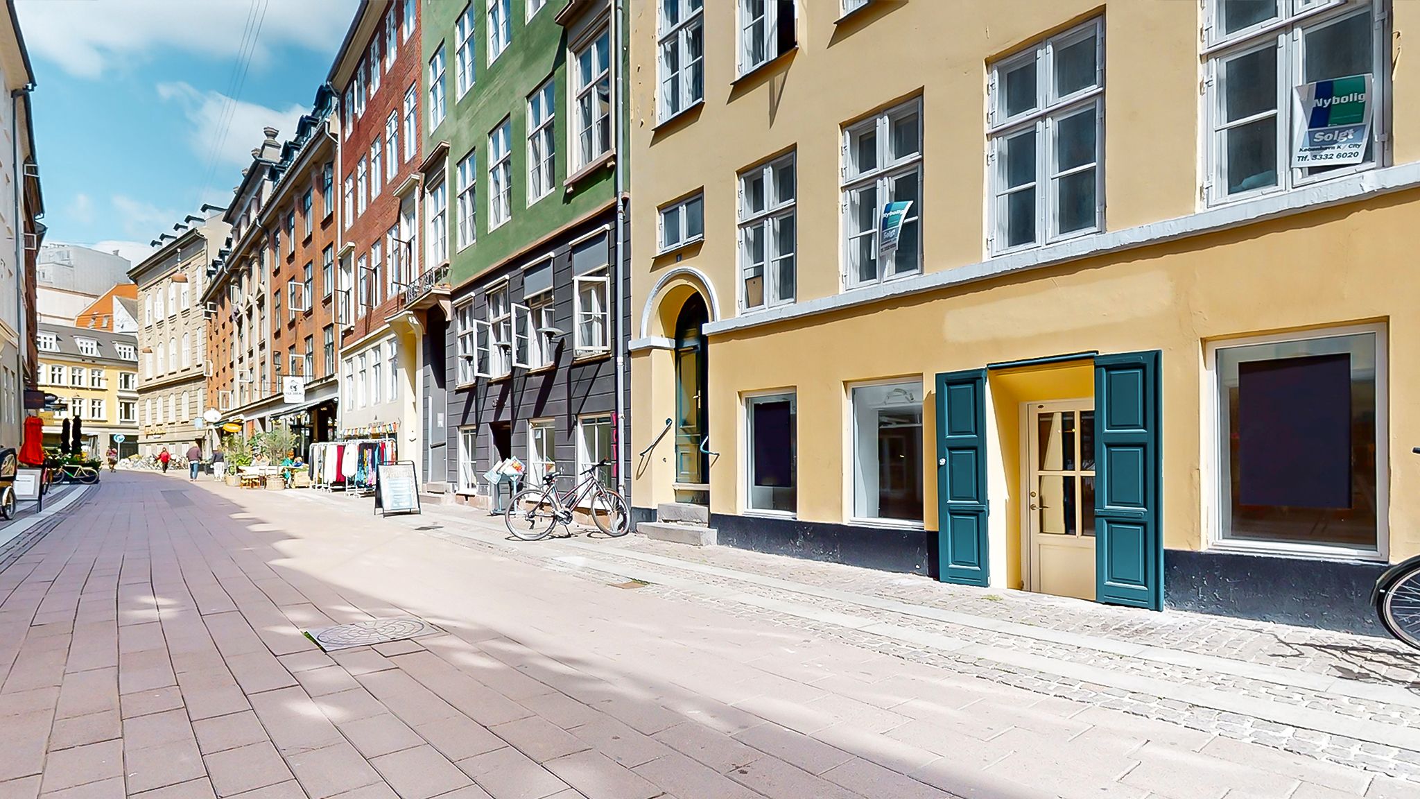 Københavnsgade med en række bygninger med butikker og vinduer, og en cykel parkeret på fortauet