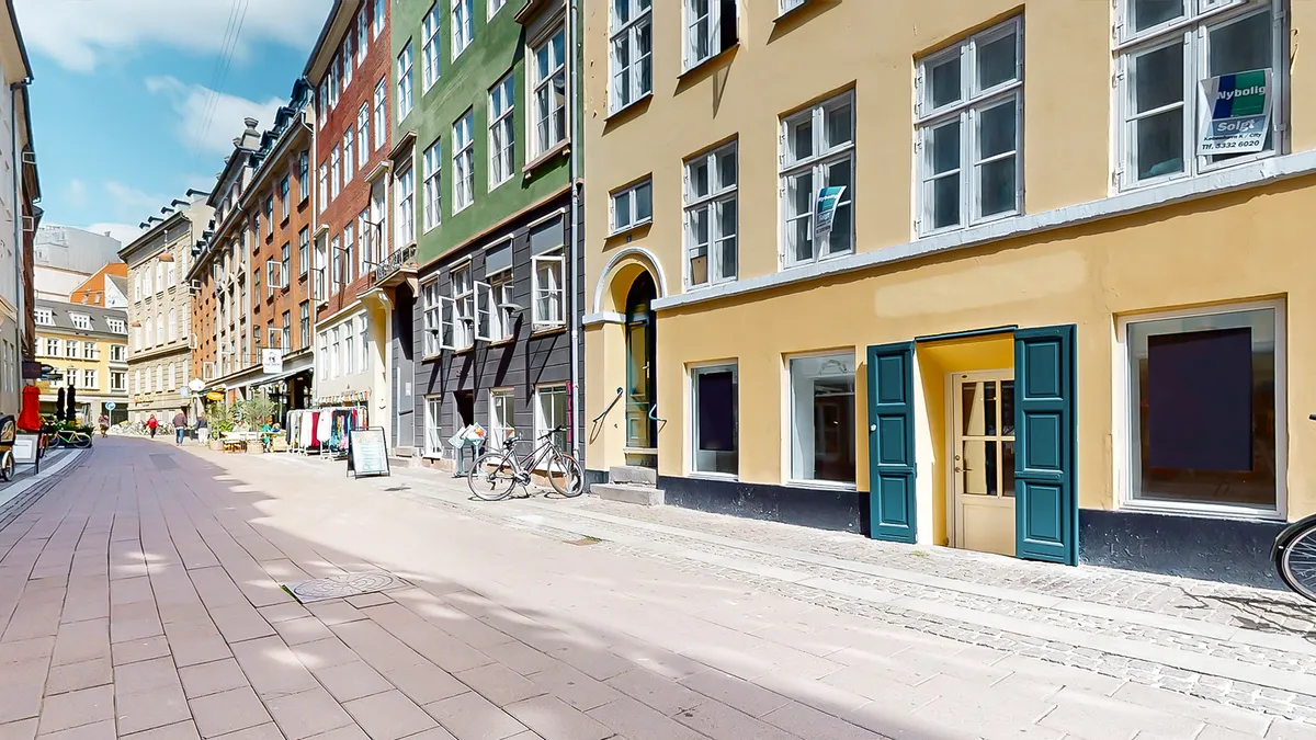 Københavnsgade med en række bygninger med butikker og vinduer, og en cykel parkeret på fortauet