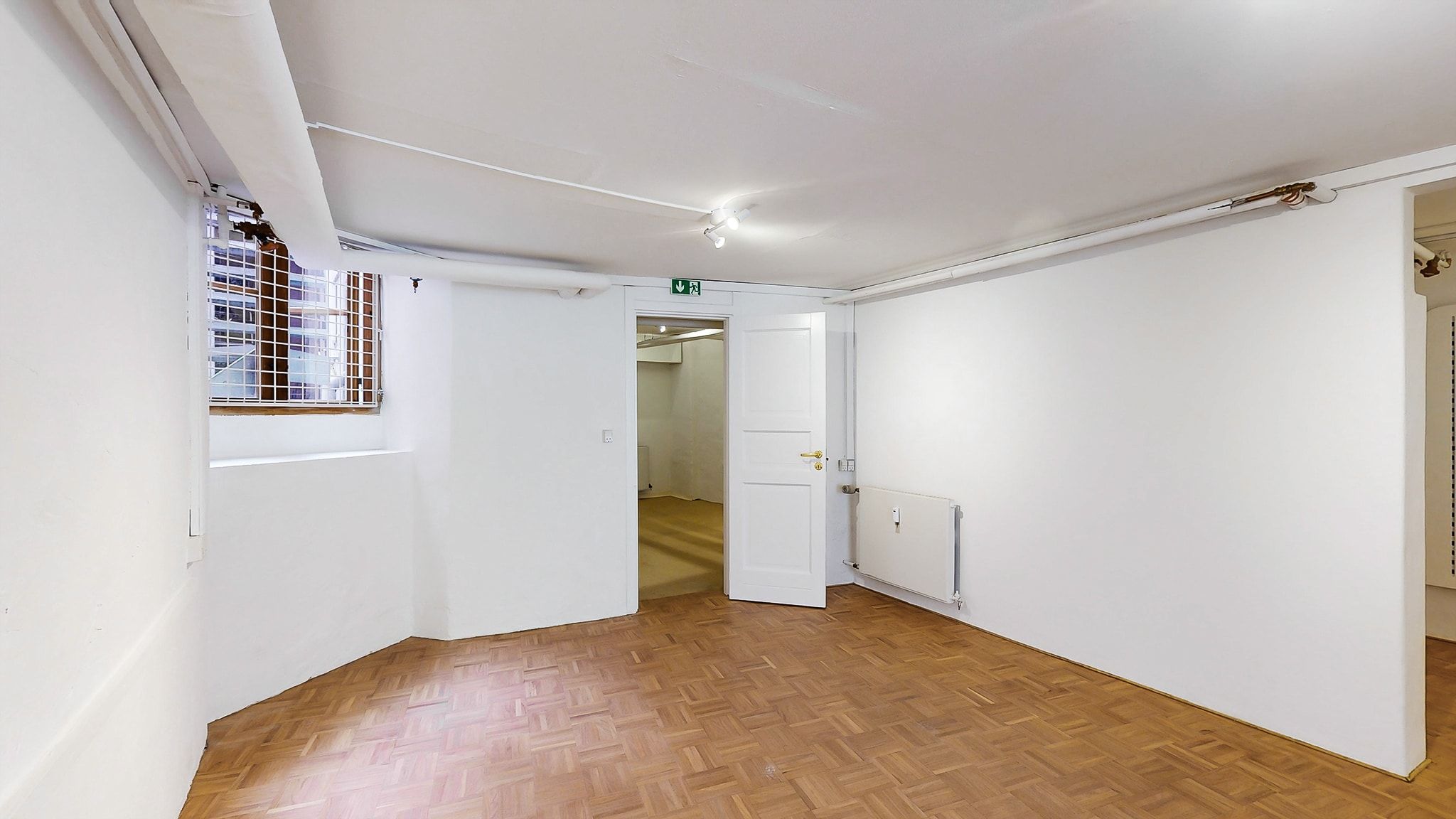 Et funktionelt butikslejemål med hvide vægge, trægulv og et slankt, hvidt dørblad til siden