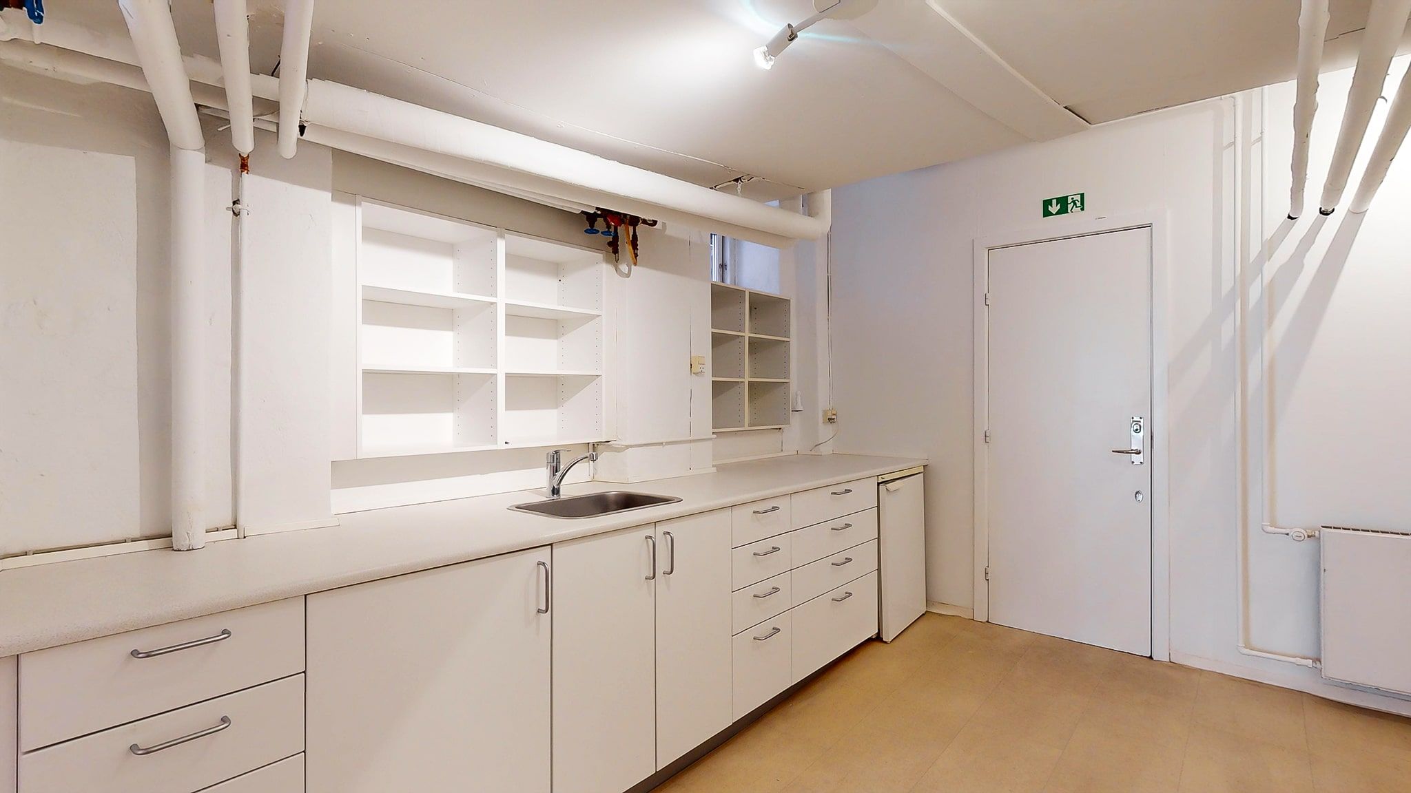 Et rent og funktionelt værksted med lyse hvide vægge og gulv samt en stor skabrække og en hvid dør