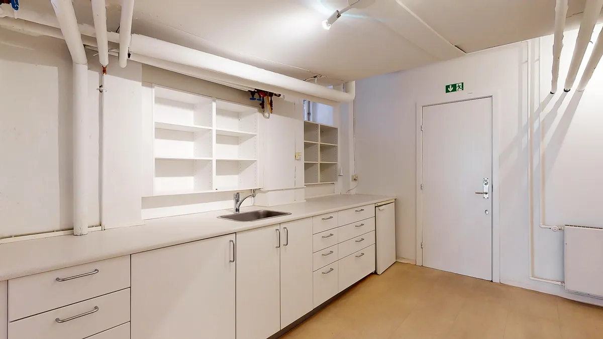 Et rent og funktionelt værksted med lyse hvide vægge og gulv samt en stor skabrække og en hvid dør