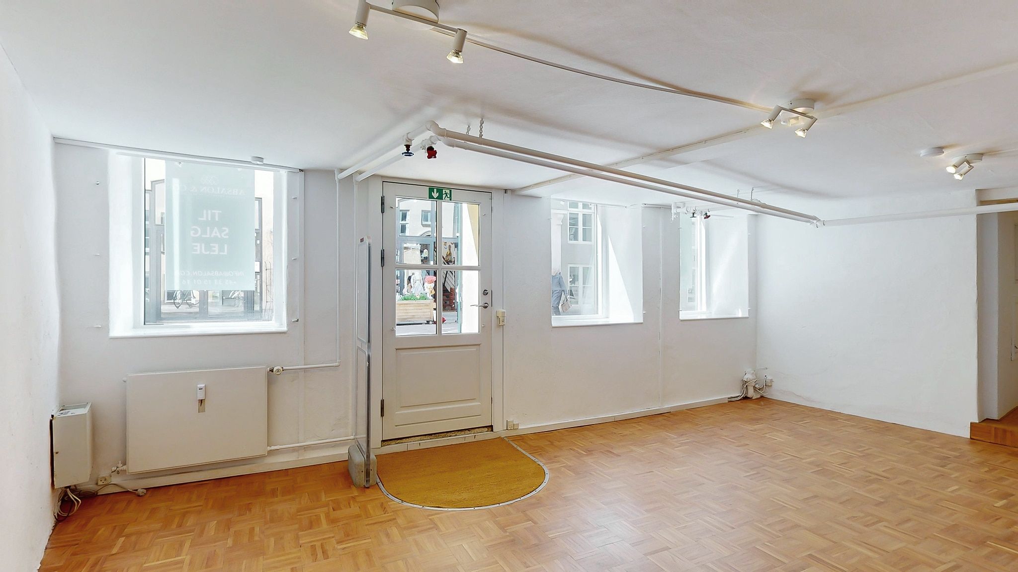 Et moderne, lyse lejlighedsværelse med parketgulv og hvide vægge samt vinduer og døre i hvidt