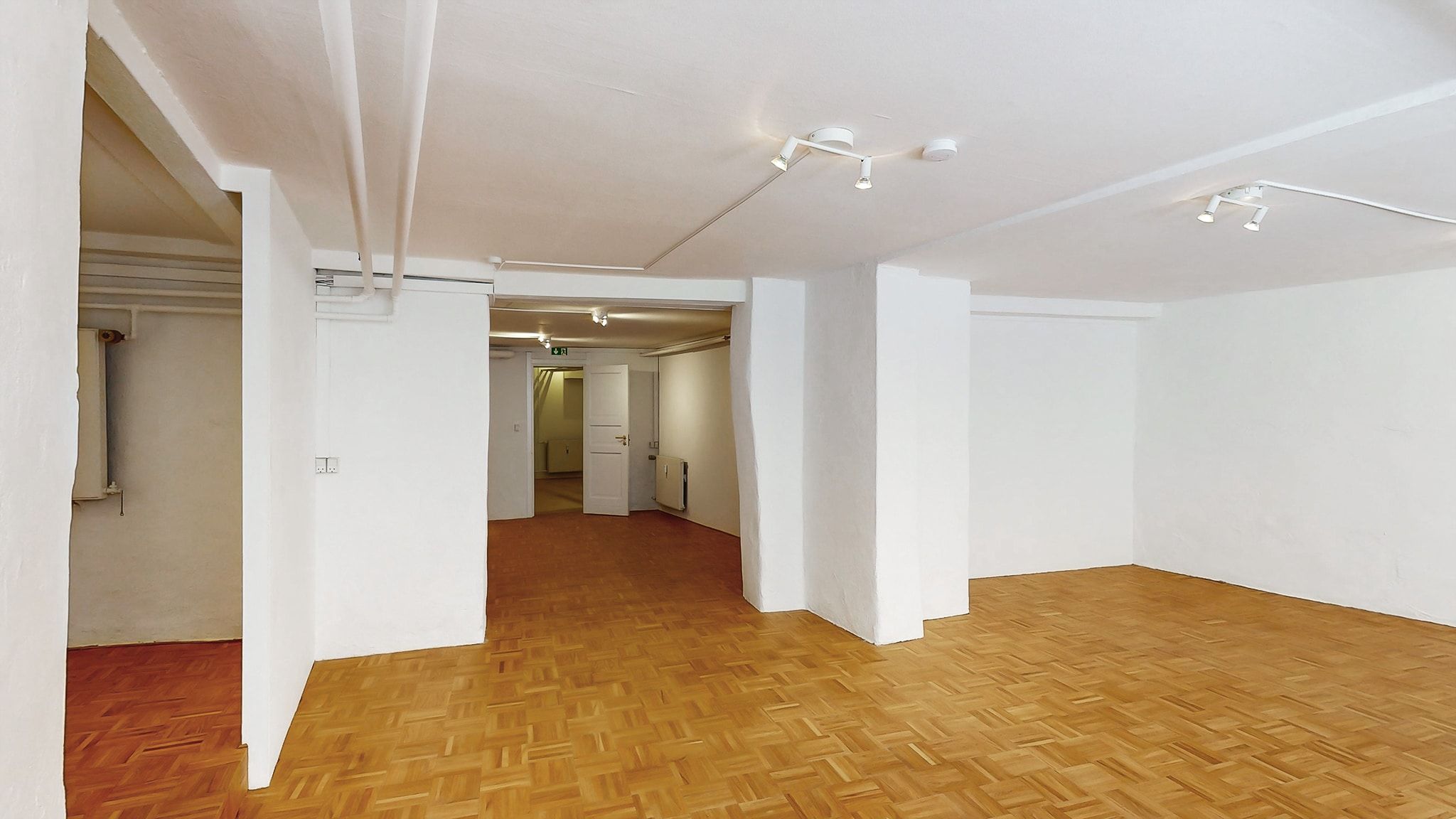 Et stort, tomt værelse med lyse hvide vægge og trægulve samt fire lysekroner hængende fra loftet