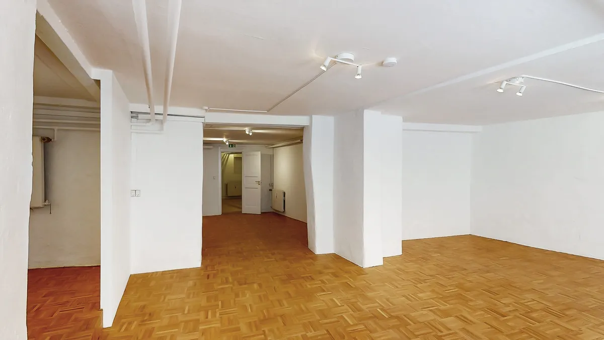 Et stort, tomt værelse med lyse hvide vægge og trægulve samt fire lysekroner hængende fra loftet