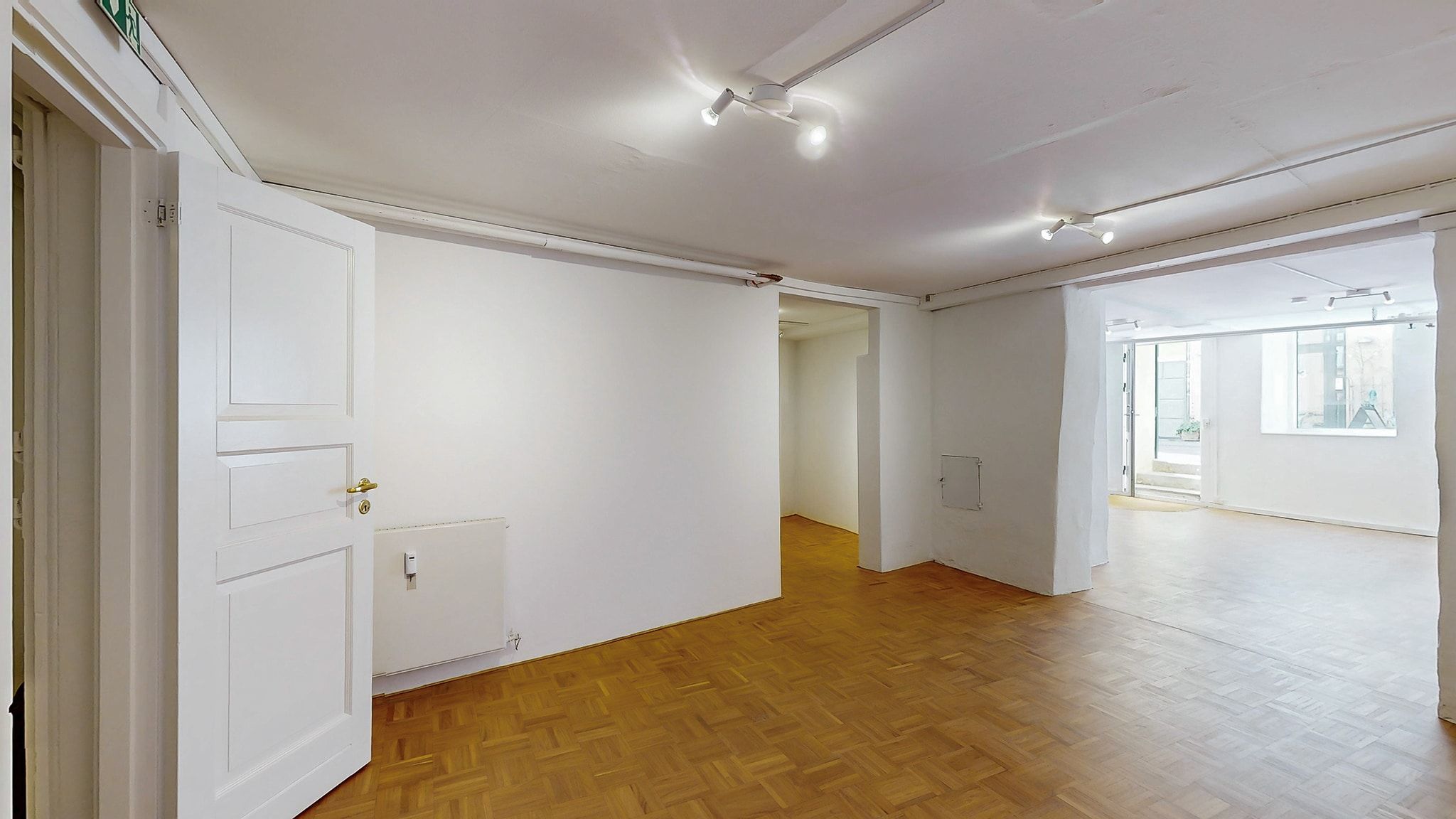 Lejlighed med lyse trægulve og hvide vægge i en stor og rummelig hall med åbne døre og moderne indretning