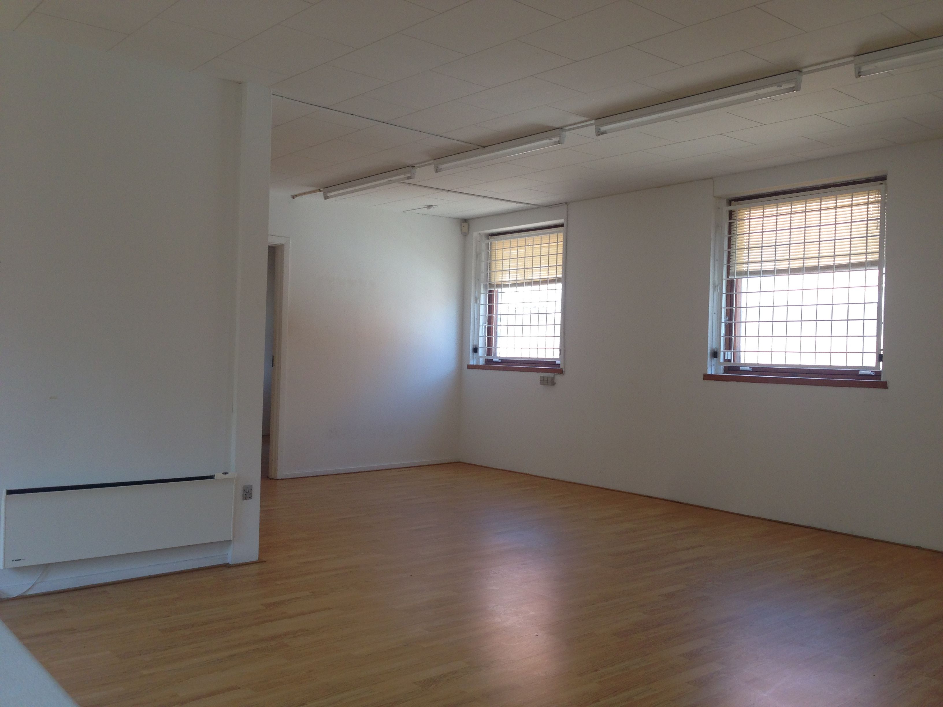 Store, lyse kontorlokaler med trægulv og store vinduer med jalousier. Moderne interiør med hvide vægge og loftsbelægning.