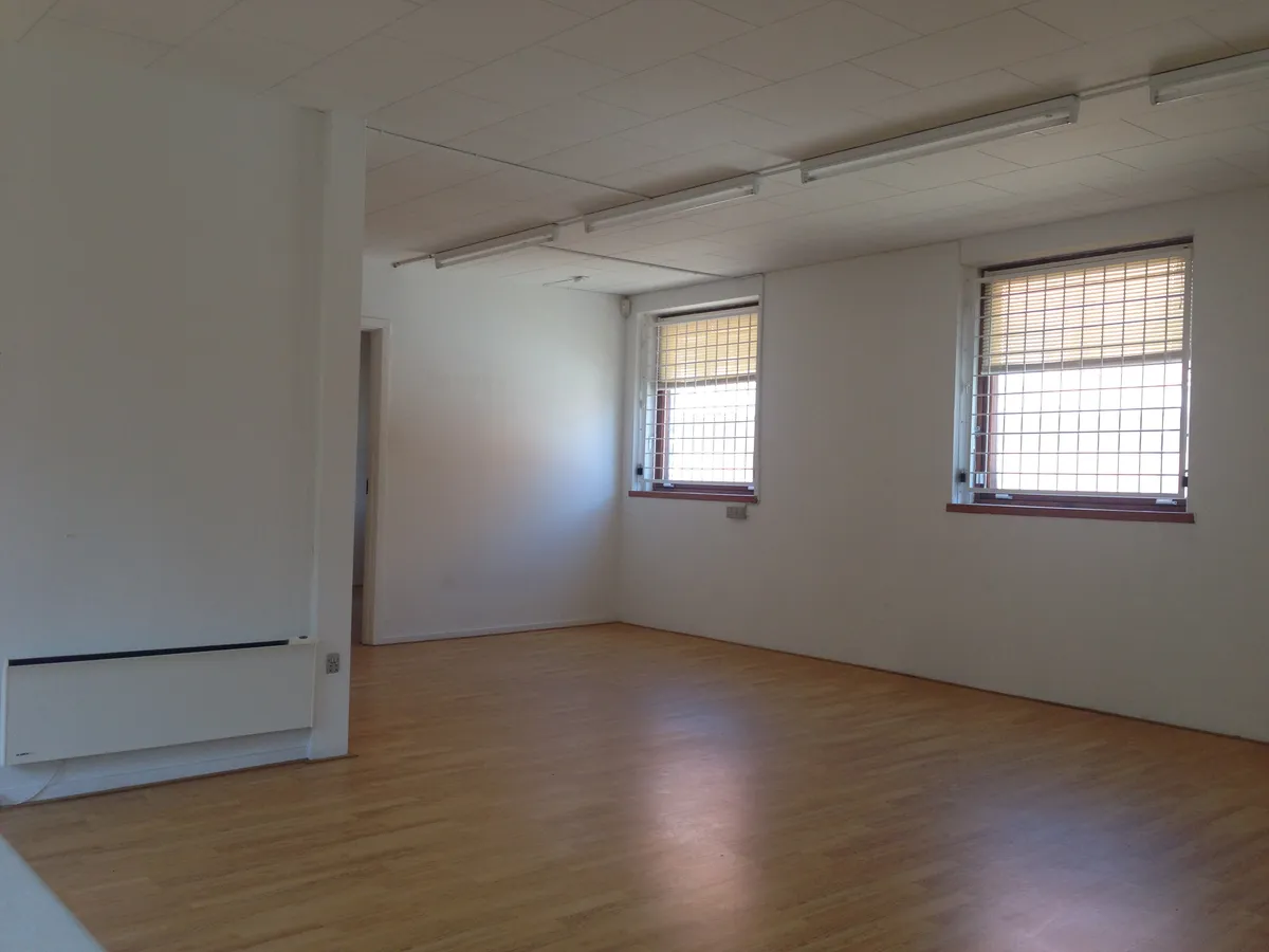 Store, lyse kontorlokaler med trægulv og store vinduer med jalousier. Moderne interiør med hvide vægge og loftsbelægning.