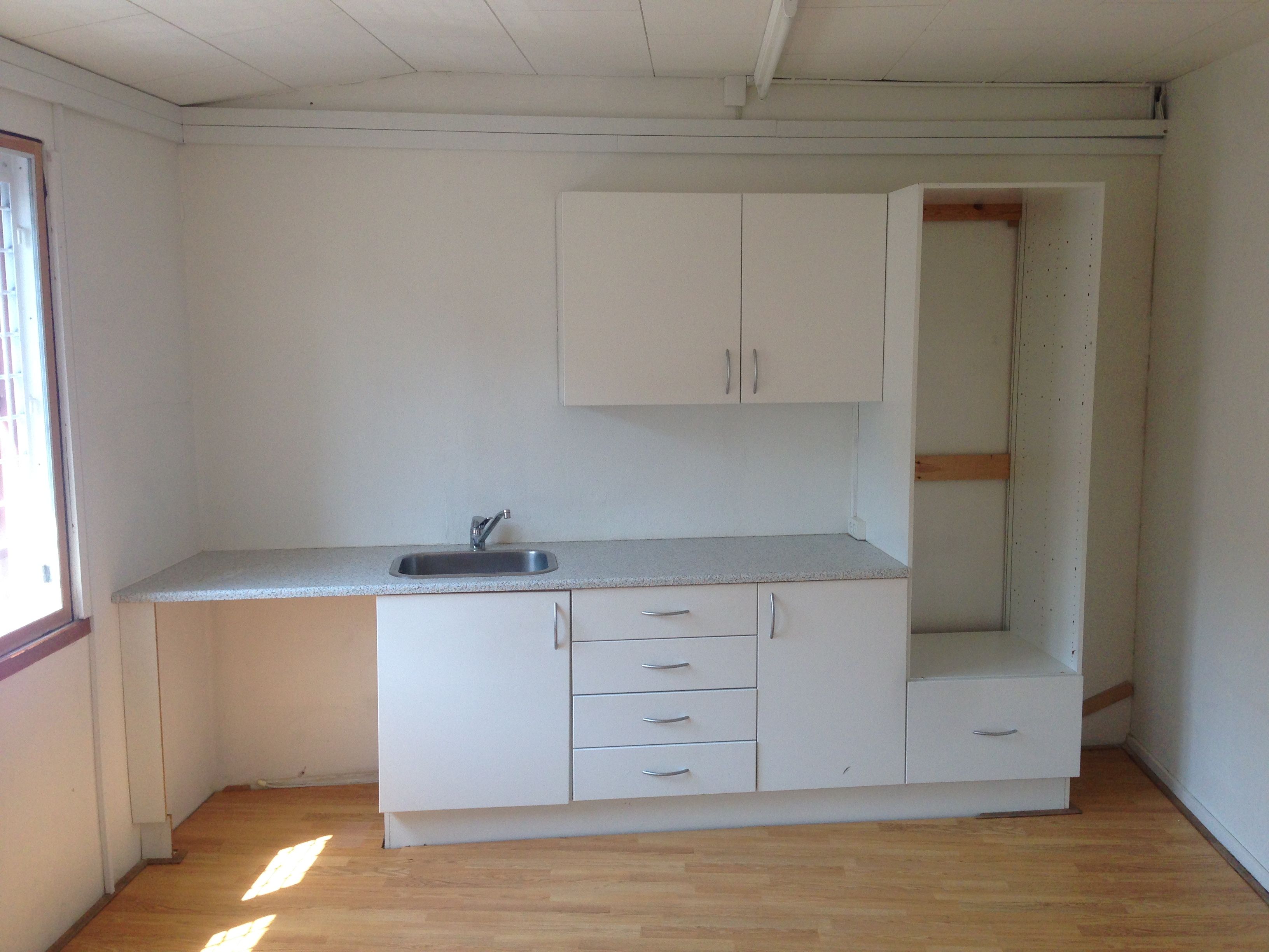 Køkken med hvide vægge og gulv samt højt tællebord og sænket vask med vandhane og højt skab med to døre