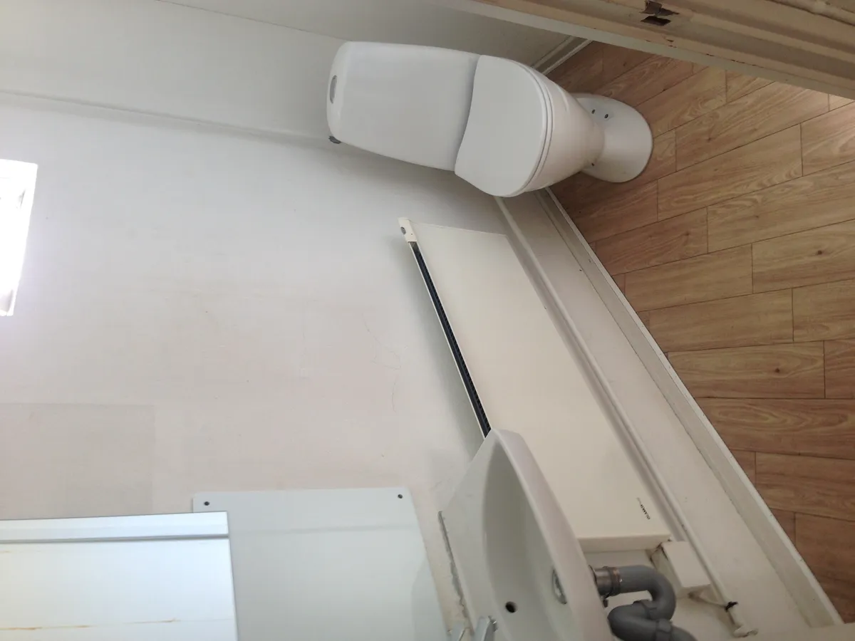 Et lille badeværelse med toilet og badekar samt gulvtæppe og radiator i hvidt