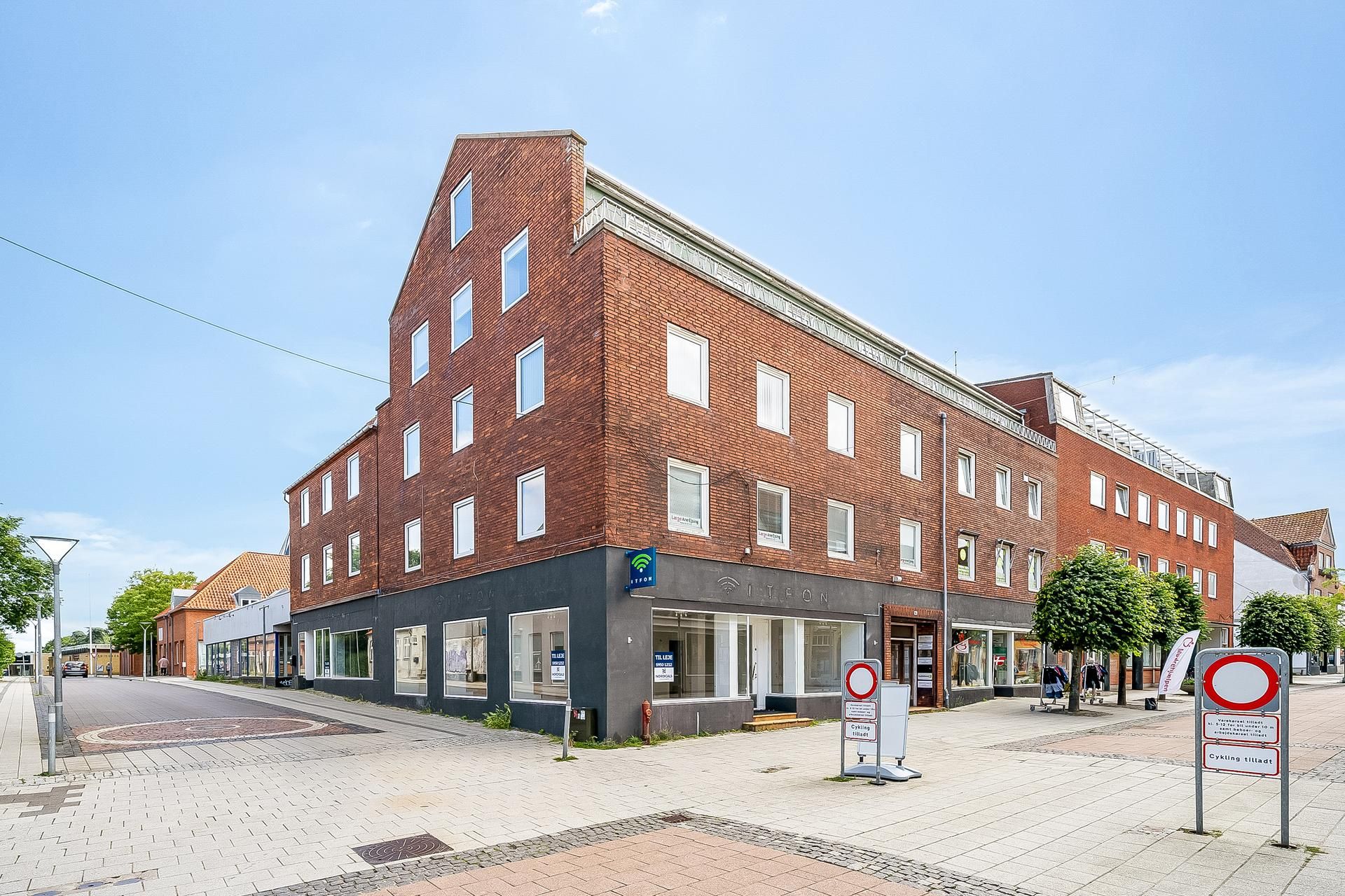 En rødmalet bygning med et skilt med teksten iTFON på første sal. På gaden står der skilte med cykling tilladt og kørsel