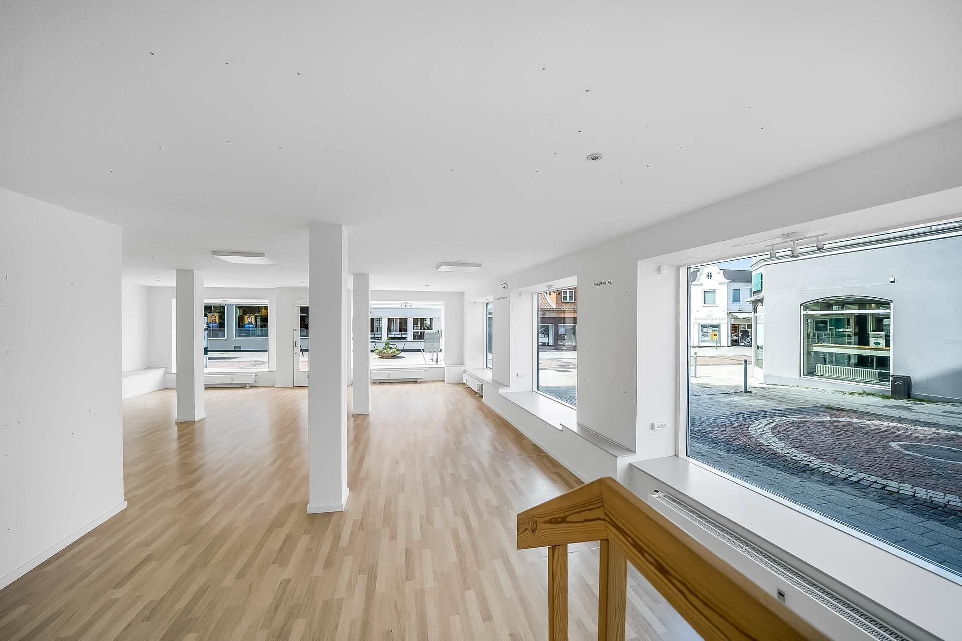 Køkken med åbent rum og lyse gulve, hvidt loft, gulvbelægning og hvide vægge samt store vinduer med udsigt til gaden