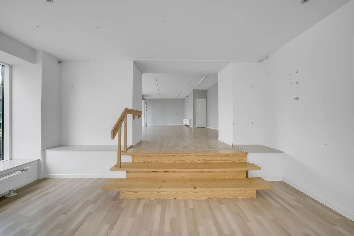 En indvendig trappe og gulv i en hvid stue med lyse trætrin og håndtag samt et hvidt gulv og vægge