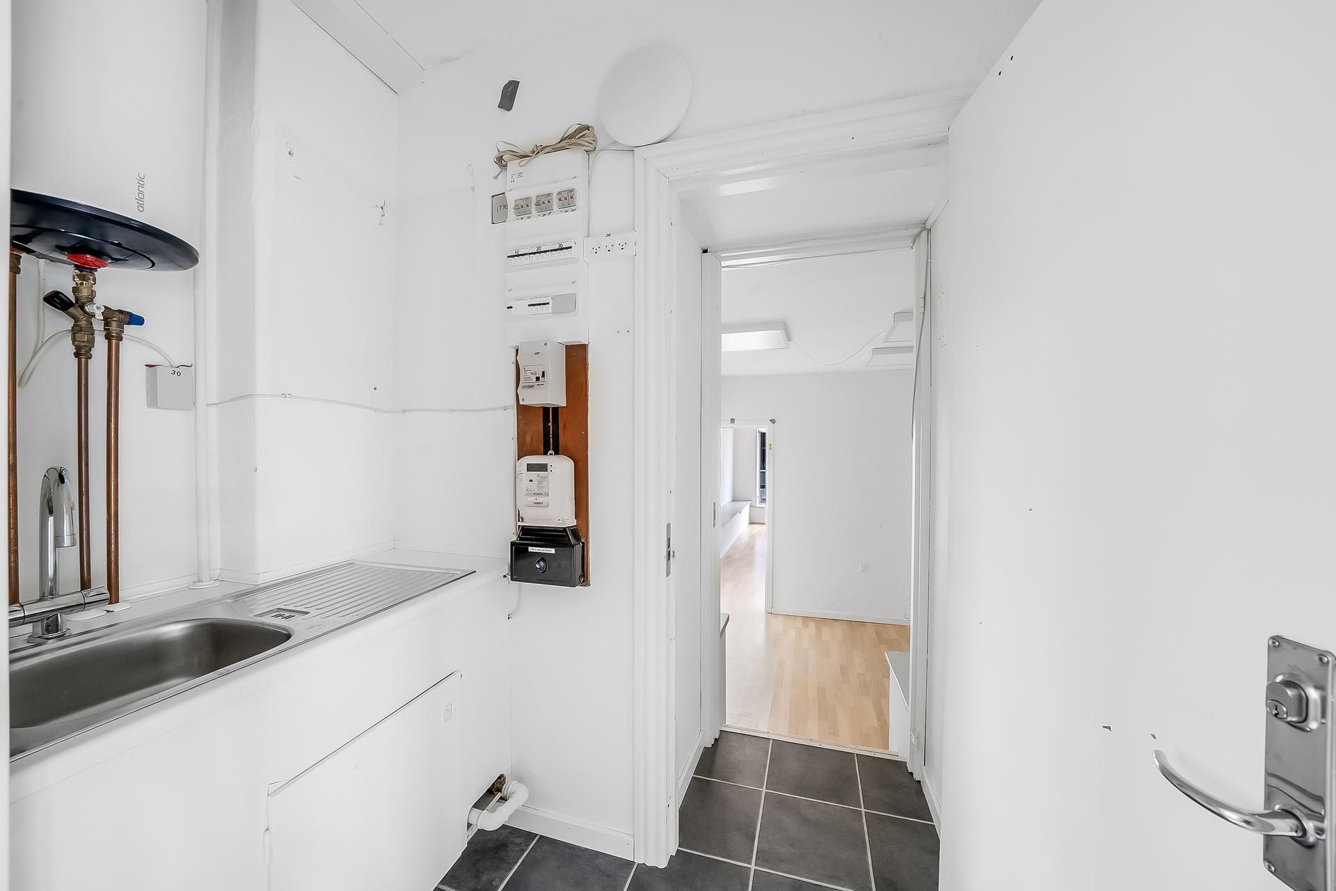 Inden for et lille køkken er der en hvid væg med en hvid dør og en tørretumbler. Der er en tæt på en vandhane og en hvid