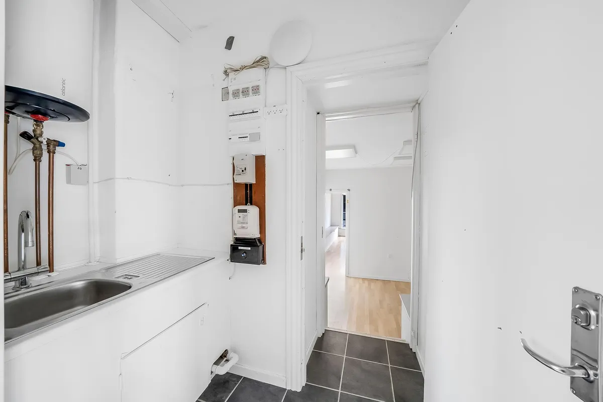 Inden for et lille køkken er der en hvid væg med en hvid dør og en tørretumbler. Der er en tæt på en vandhane og en hvid