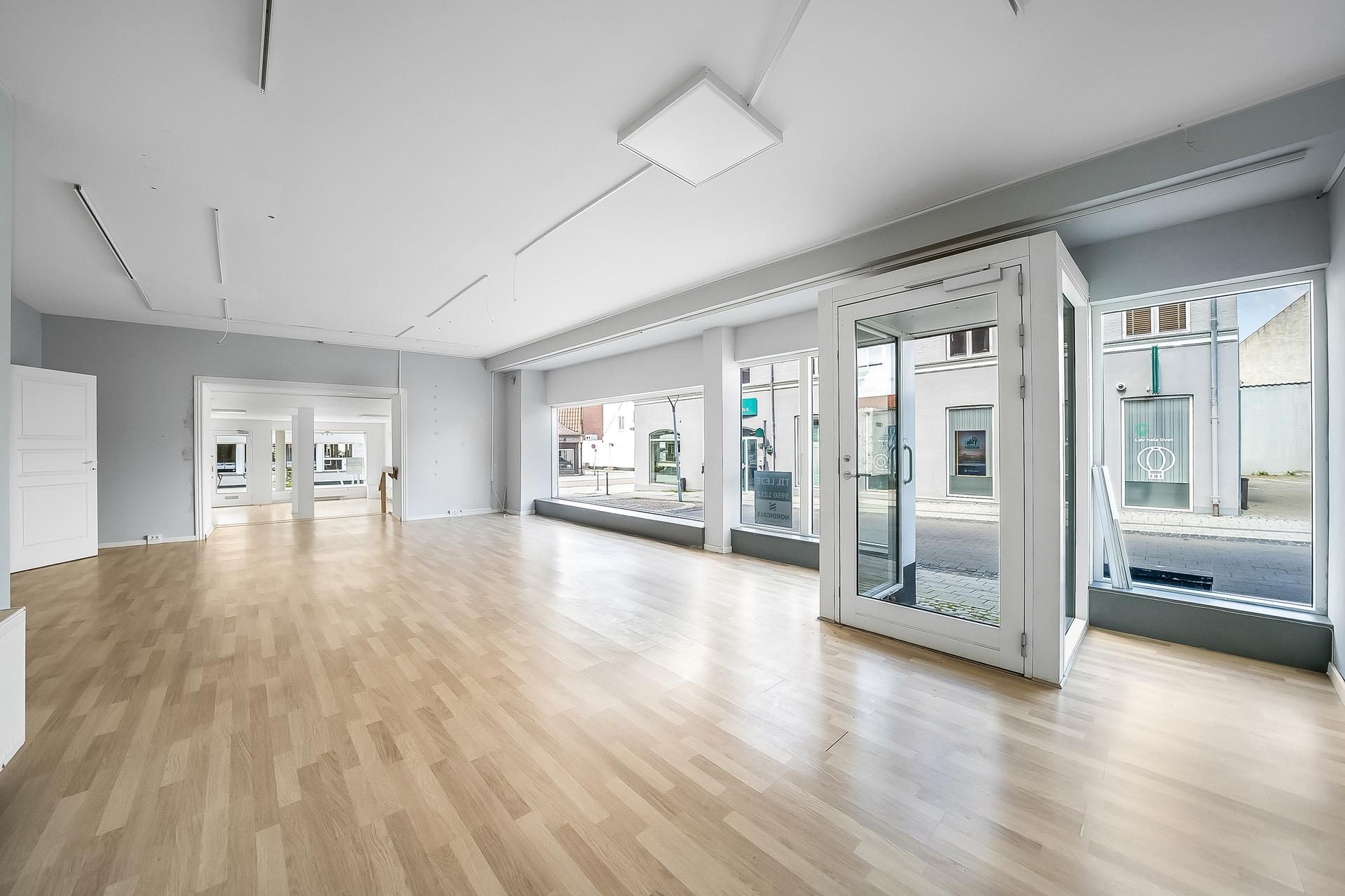 Store, lyse vinduer med hvide døre og en stor åbning i gulvet og loftet. Der er hårdt trægulv og hvide vægge.