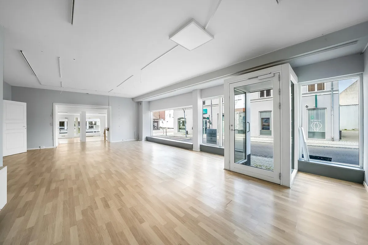 Store, lyse vinduer med hvide døre og en stor åbning i gulvet og loftet. Der er hårdt trægulv og hvide vægge.