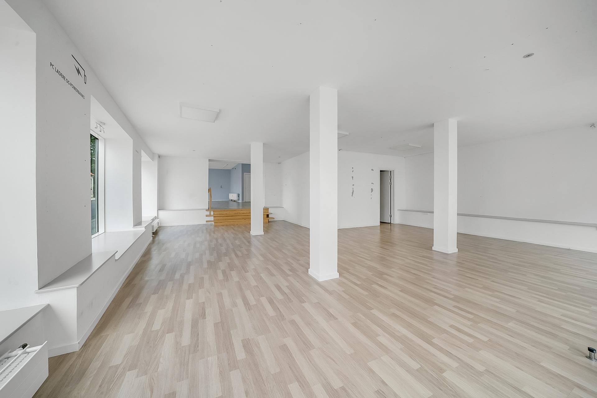 En tom indvendig lokale med hvide vægge og højloft, møbler og vinduer med glas samt højloftsventilation og hvidt gulv.