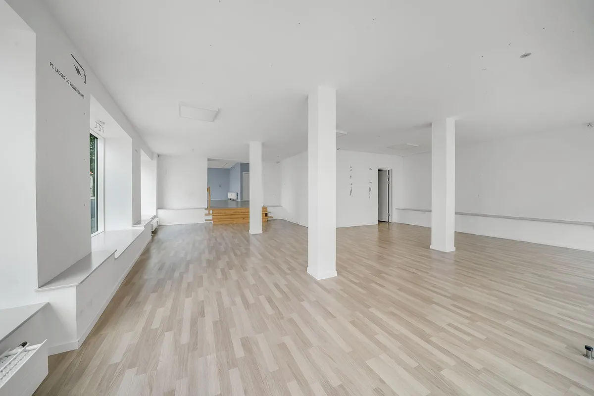 En tom indvendig lokale med hvide vægge og højloft, møbler og vinduer med glas samt højloftsventilation og hvidt gulv.