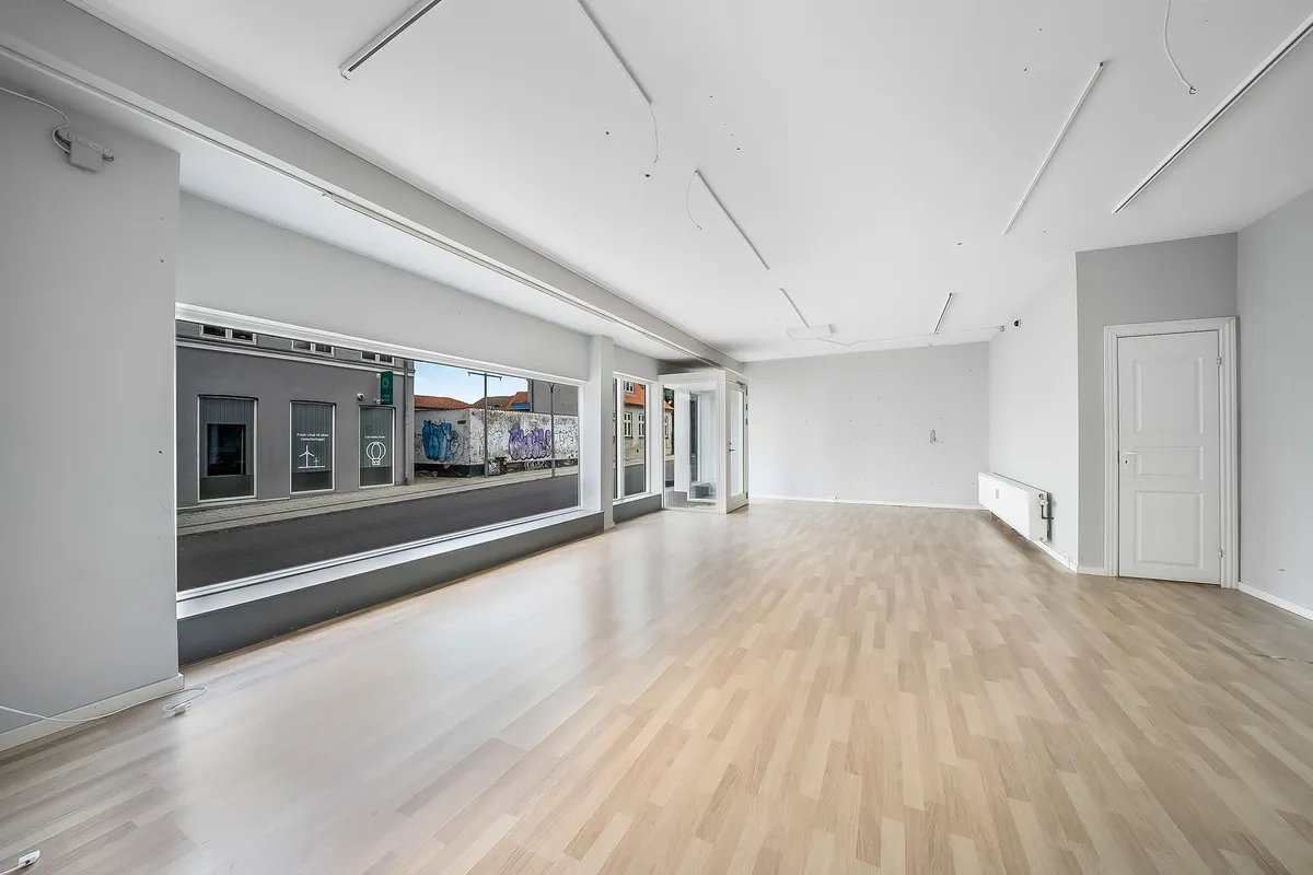 En stor og lys businesslokale med hvide vægge, lysegrå gulv og hvide døre samt store vinduer med udsigt til gaden med en