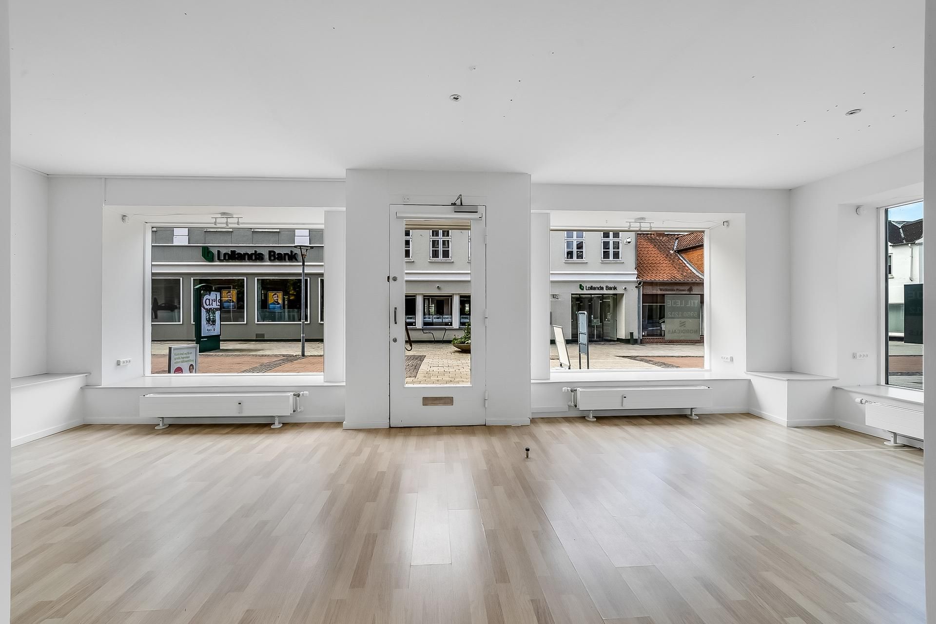 En moderne butik med hvide vægge, trægulv og store ruder til Algade i Vordingborg med Lolands Bank i baggrunden