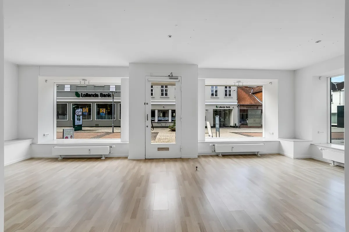 En moderne butik med hvide vægge, trægulv og store ruder til Algade i Vordingborg med Lolands Bank i baggrunden