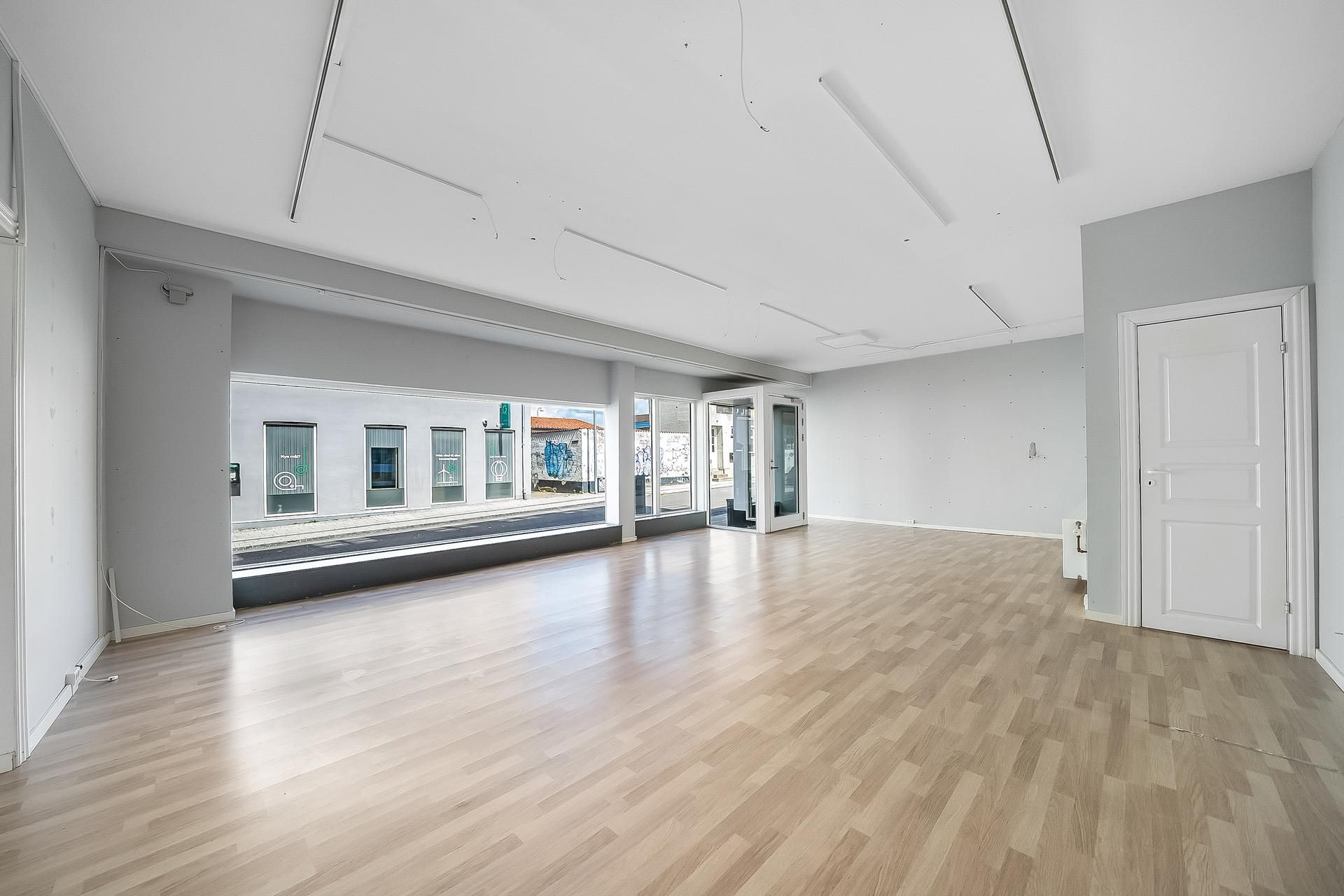 Store lokaler med højloft og lysegult gulv. Store vinduer med udsigt til hovedgaden. En dør er åben og leder ind i et tomt