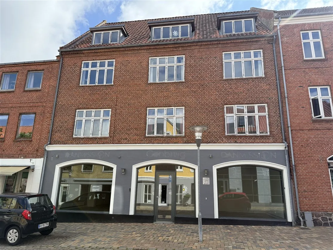 Butikslokaler med store glasruder og moderne indgang i Ringe Centrum, med biler parkeret udenfor
