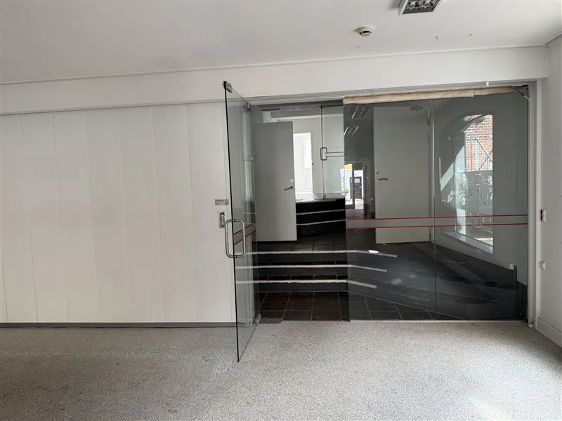 Erhvervslejlighed med moderne glasdøre og indvendige trapper til øverste etage i et velholdt bygningskompleks