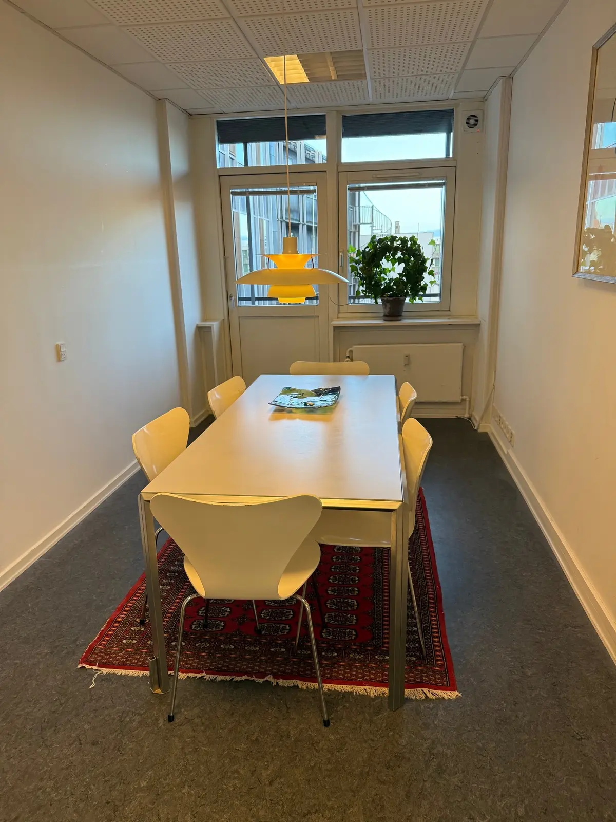 Kontorlokale med lyse, hvide vægge og moderne møbler, herunder en hvid spisestue med lysestole og et bord med en plante og