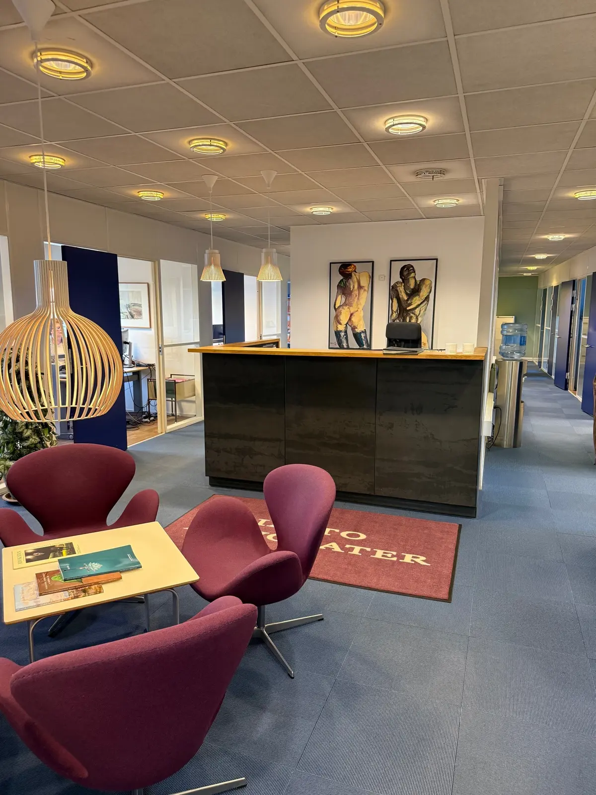 Moderne lobby med reception, borde og stole, lys og kunstværker på væggen, en ståbord og en ståplade med teksten "To Water"