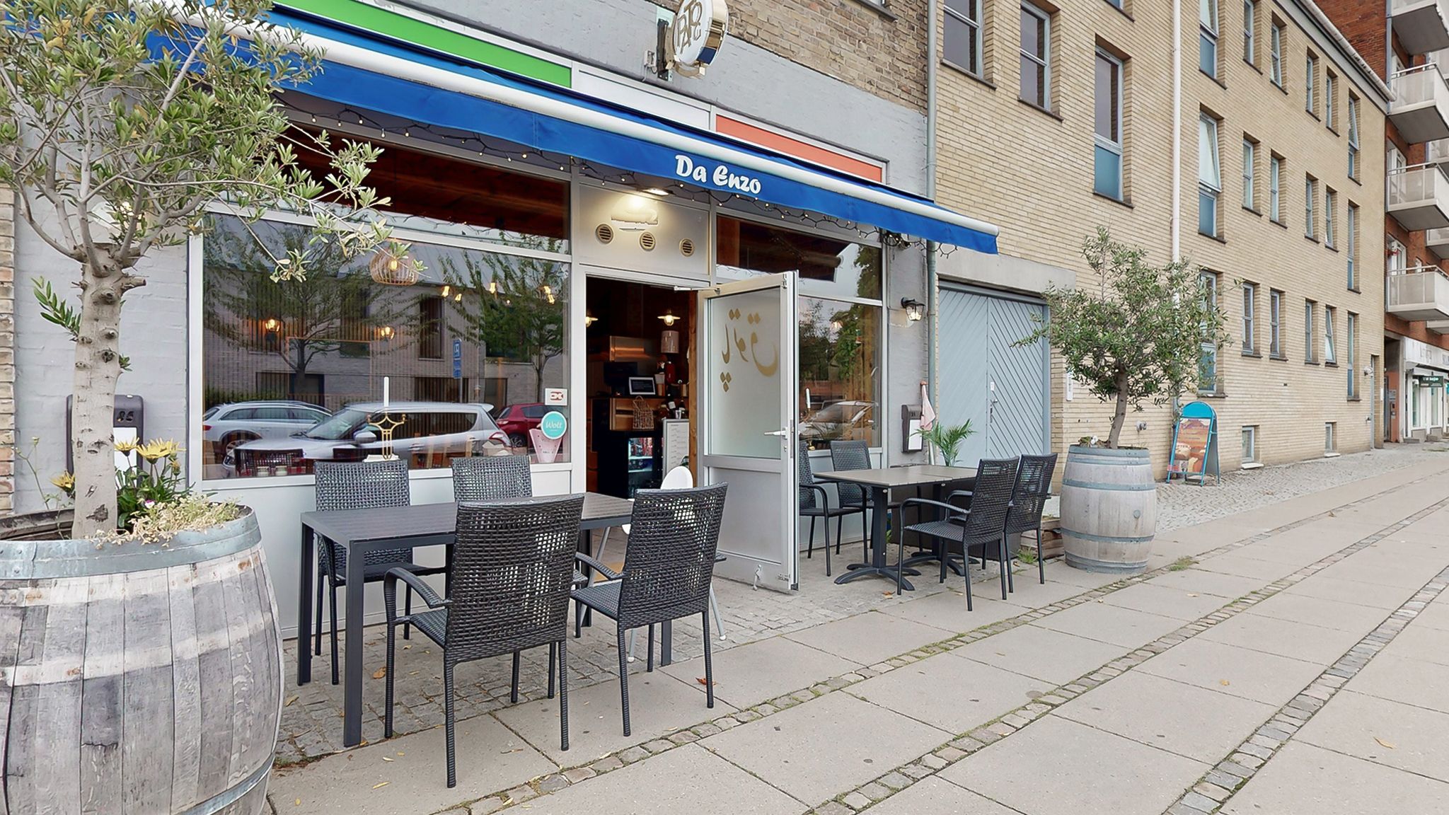 En restaurant med et blåt aurikke udenfor og træplanter og stole og borde på fortauet