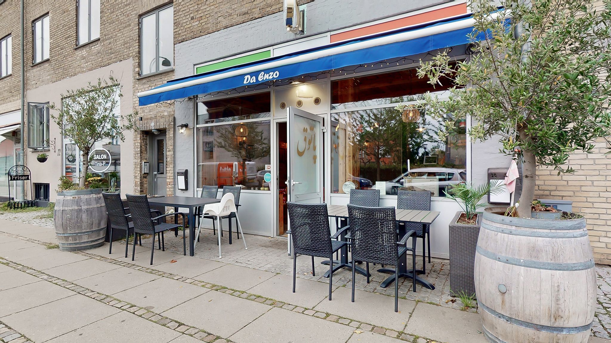 Hvidt og blåt udsmykket café med bord og stole samt træfælder med planter udenfor