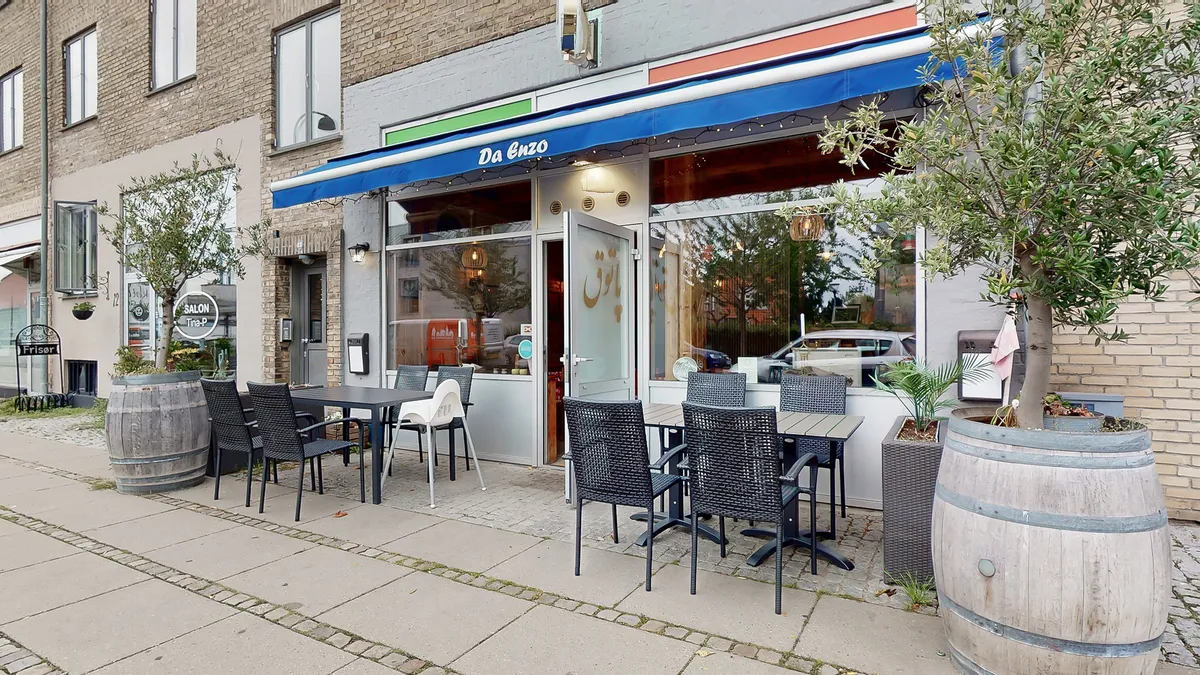 Hvidt og blåt udsmykket café med bord og stole samt træfælder med planter udenfor