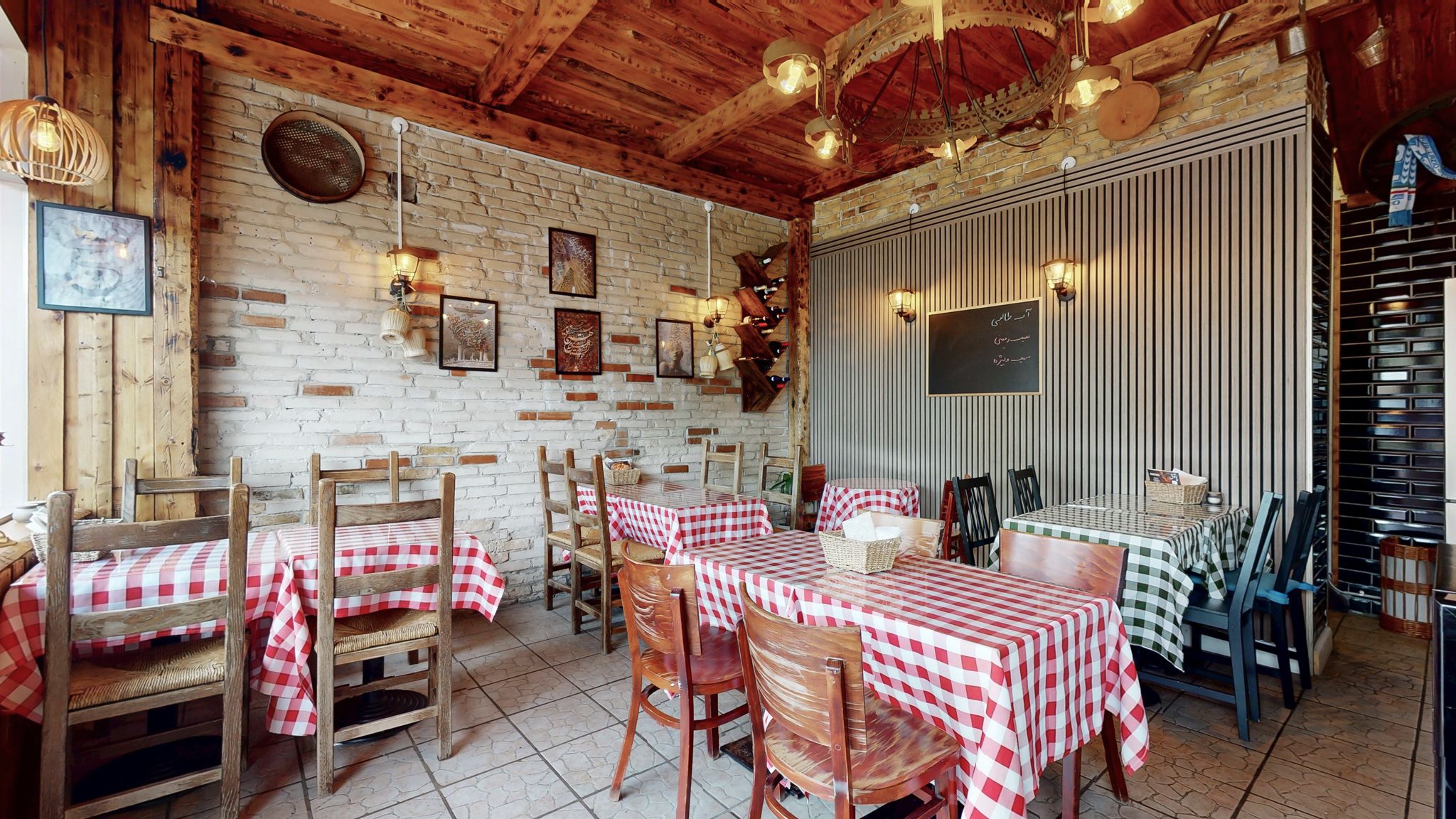 Restaurant med trævægge og loft, røde og hvide borde med klud, lysekroner og gamle malerier på væggen, og en menutavle med