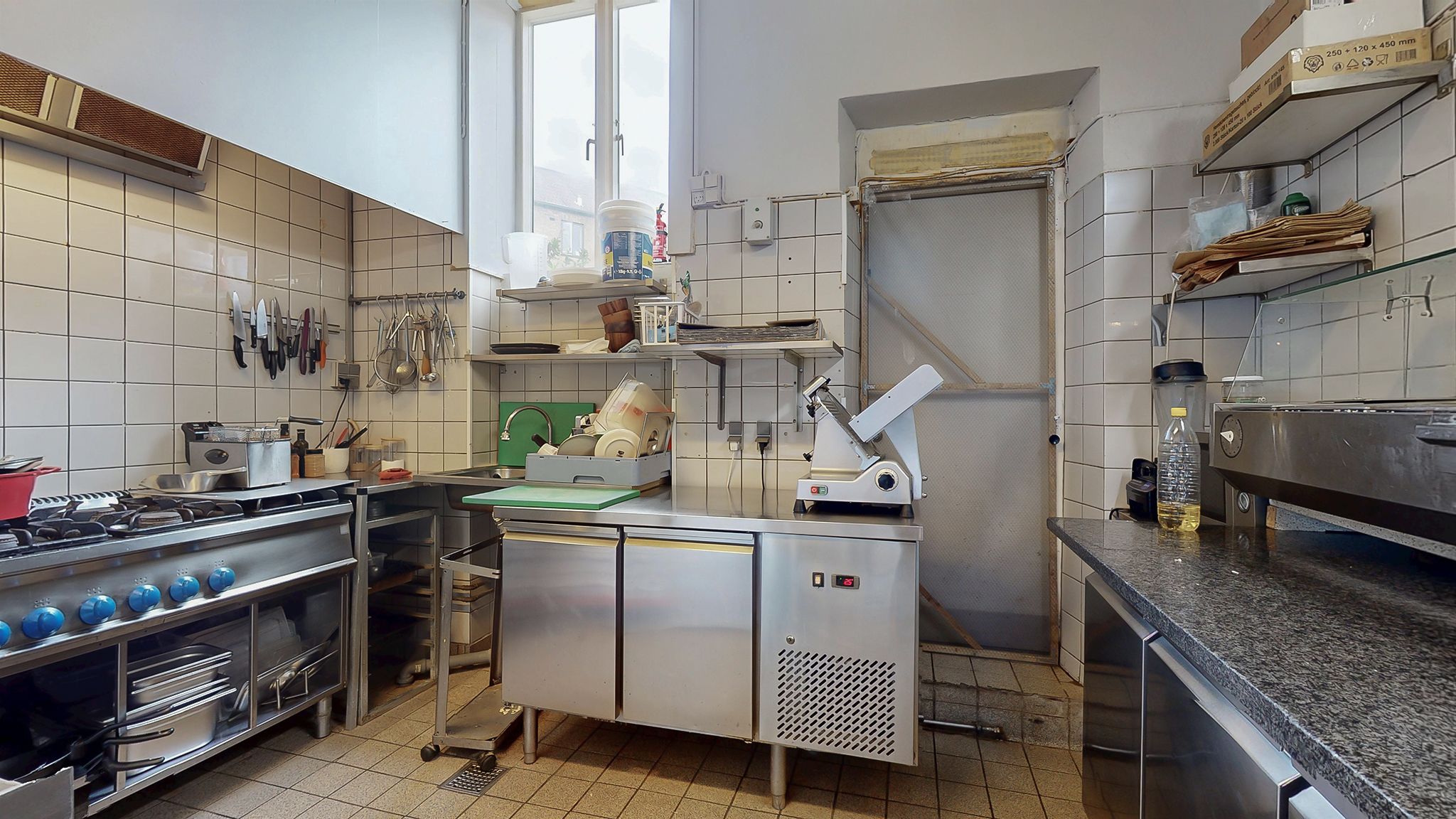 Et stort køkken med ovn, gaskomfur, slibemaskine, køleskab og flere apparater til madlavning og opbevaring