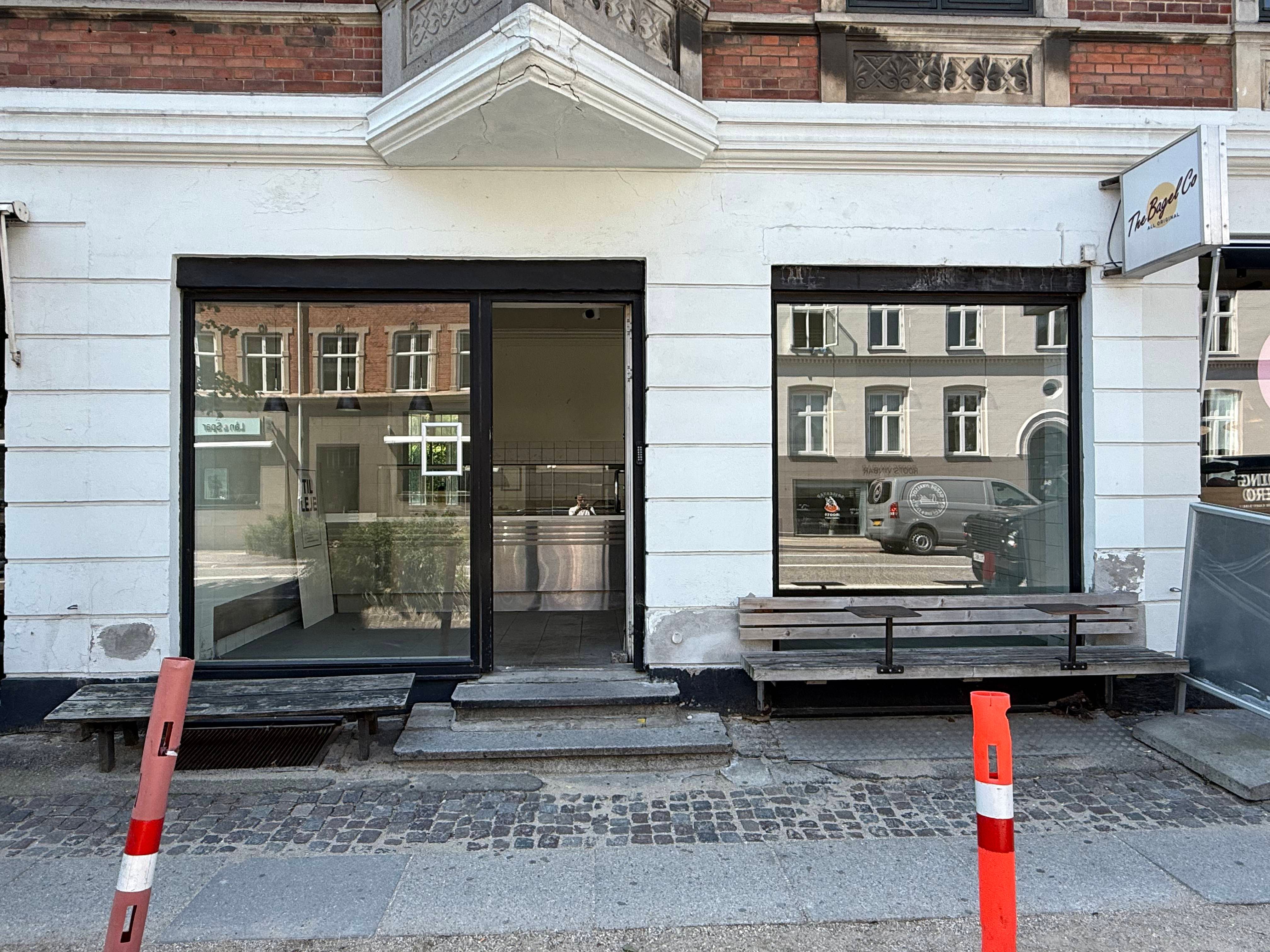 En bygning med en take-away butik kaldet The Bagel Co og udendørs bord og stole