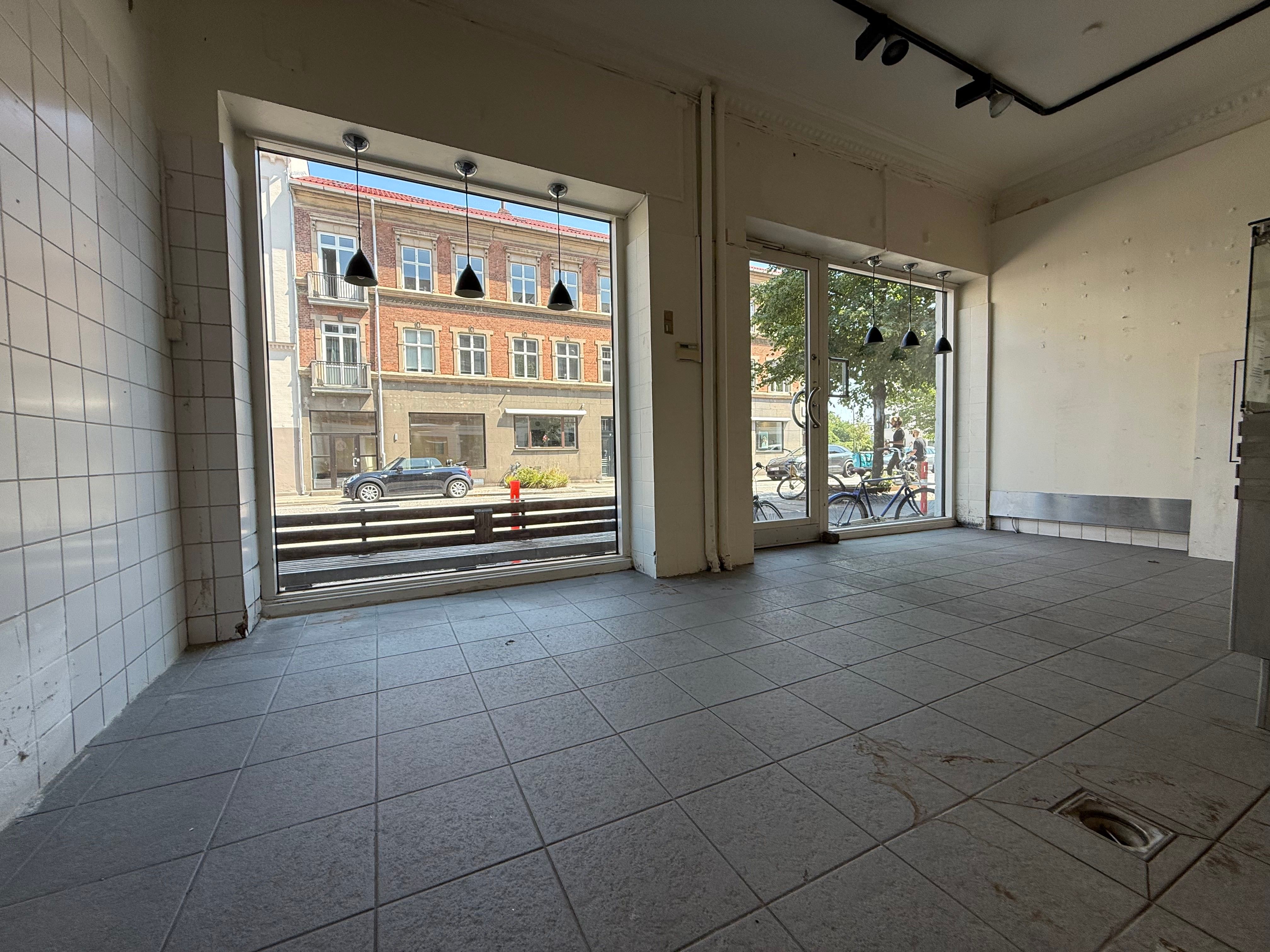 En tom forretningslokale med hvide vægge og store glasruder og døre i et populært kvarter