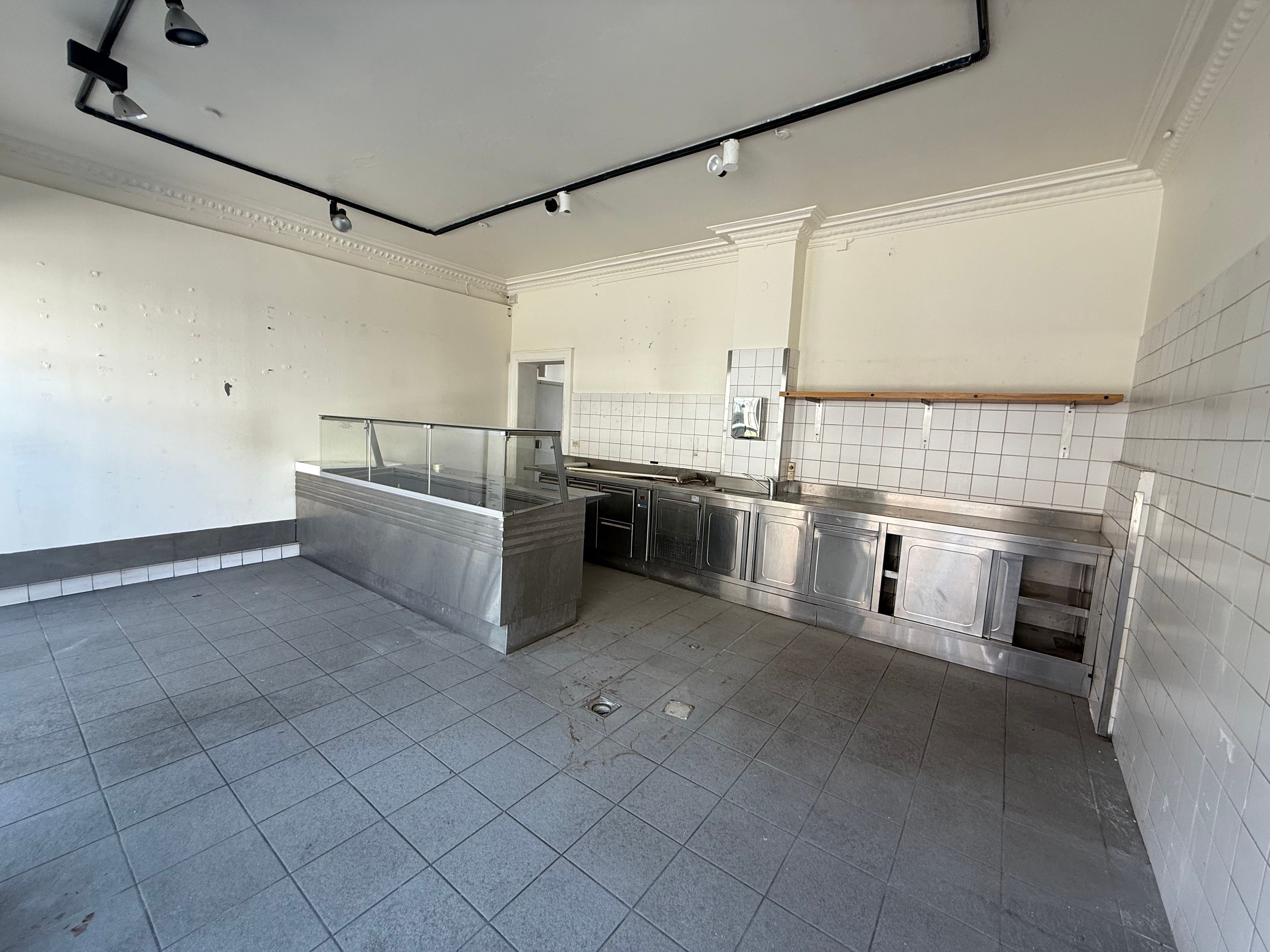 En stor, tom køkkenlokal med skrald, flere skabe, udstyr, en høj bar og en dør i baggrunden