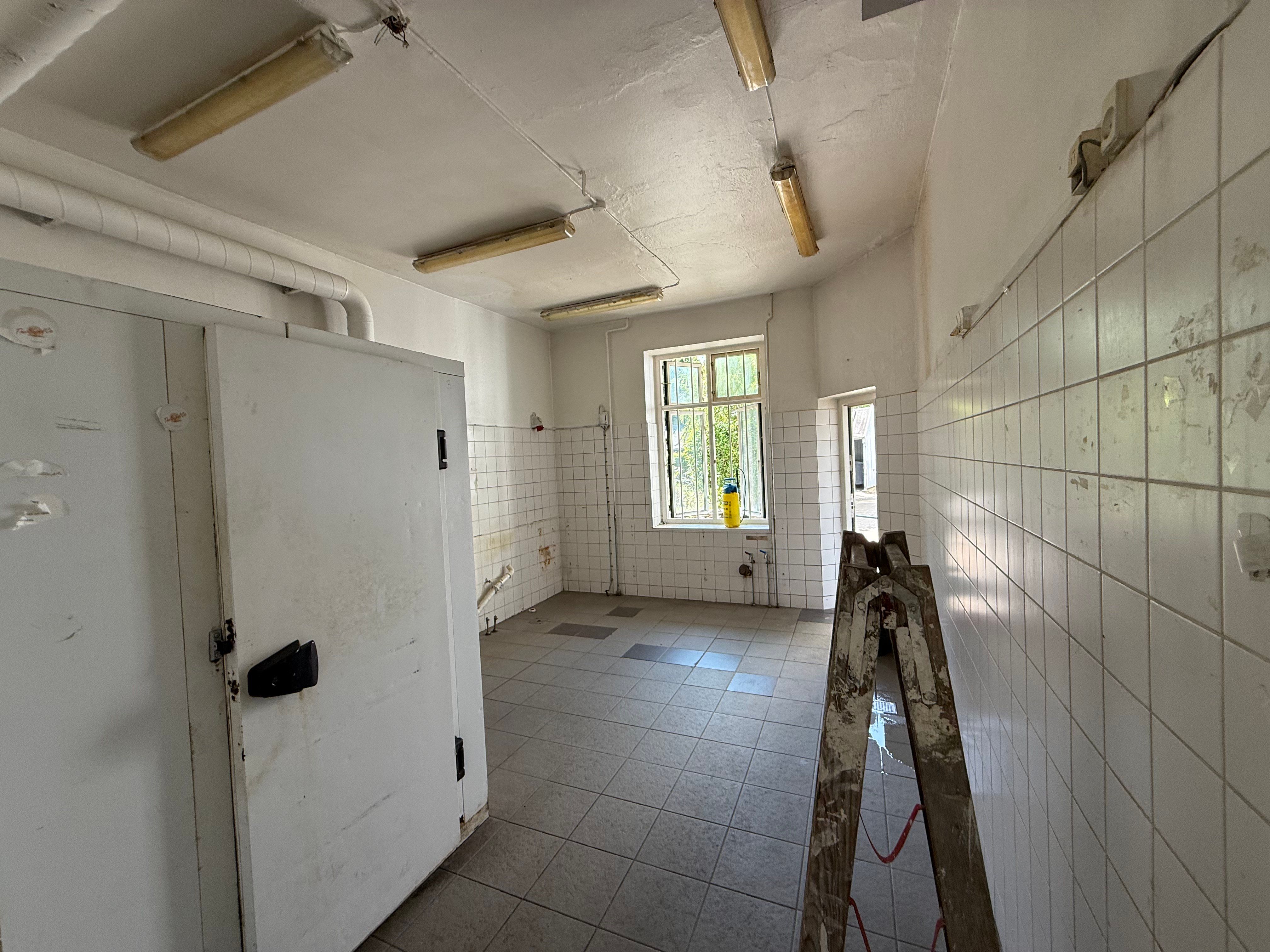 En stor, hvid fryseren står i et køkken med en stor skur og et vindue med udsigt til haven