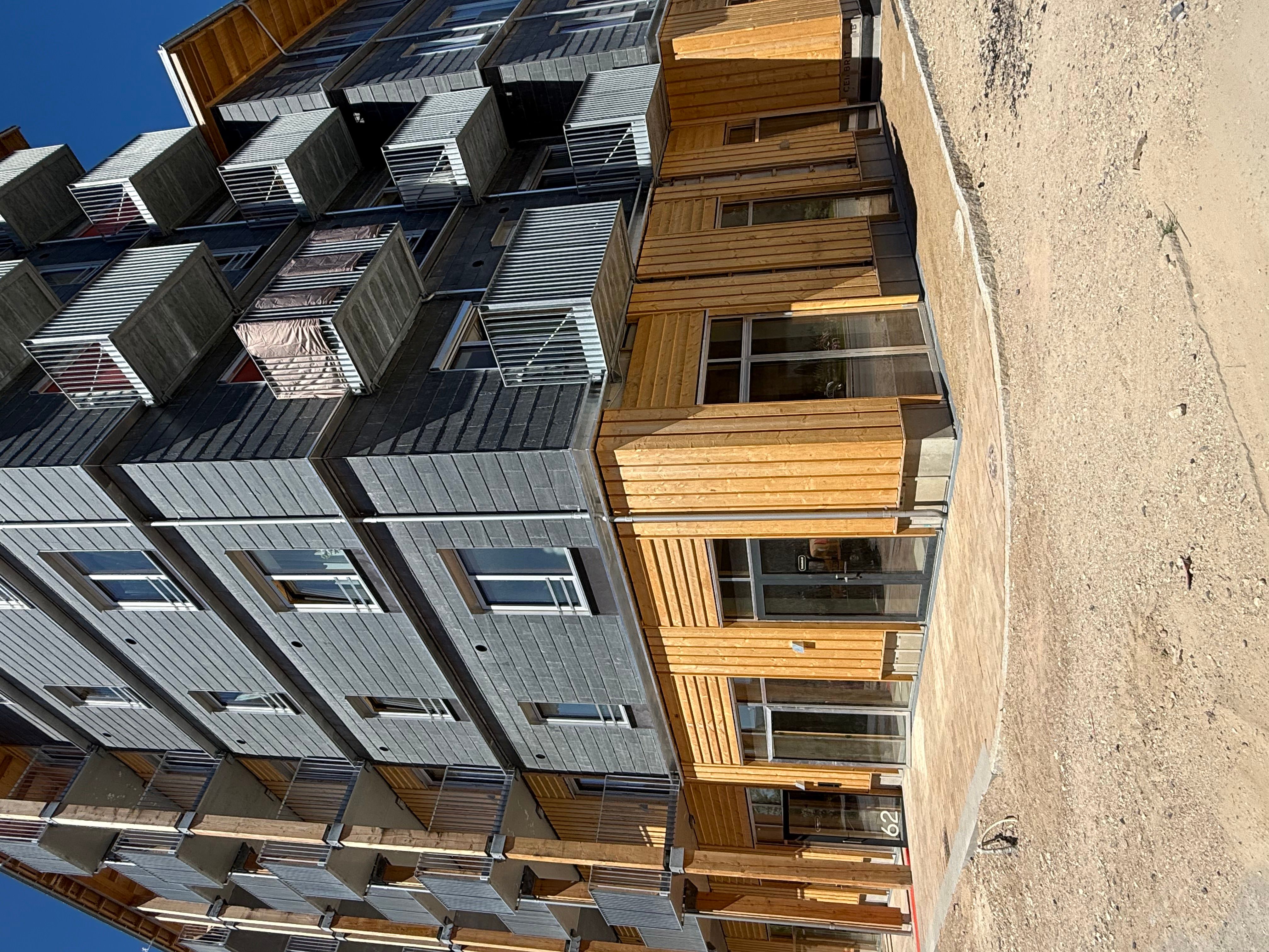 Bygning med lyse, træpaneler og metalelementer samt mange vinduer og balkoner