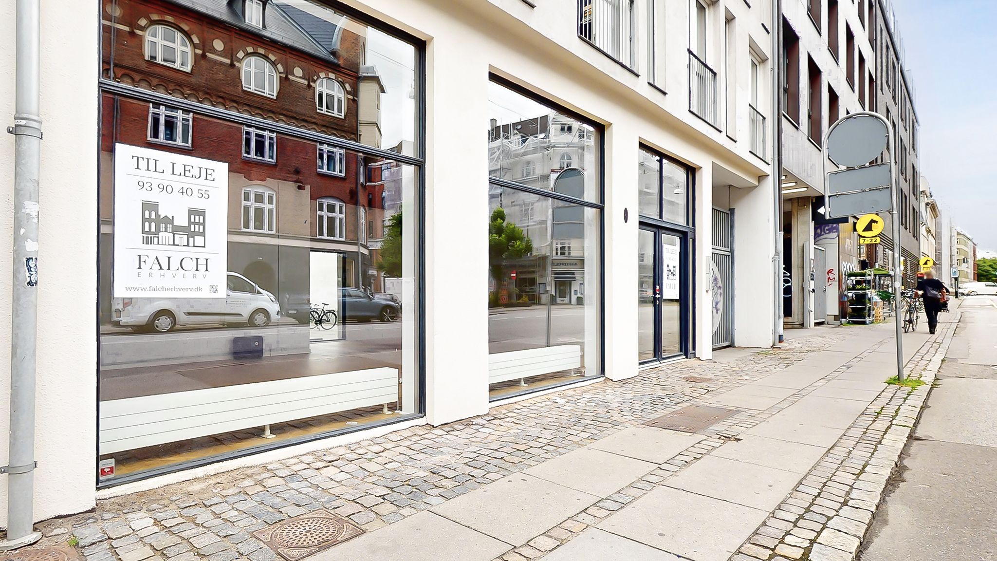 Lejemål med vinduer mod gaden, fuld af refleksioner af biler og bygninger. Tegn med adressen og www.falcherverv.dk. En