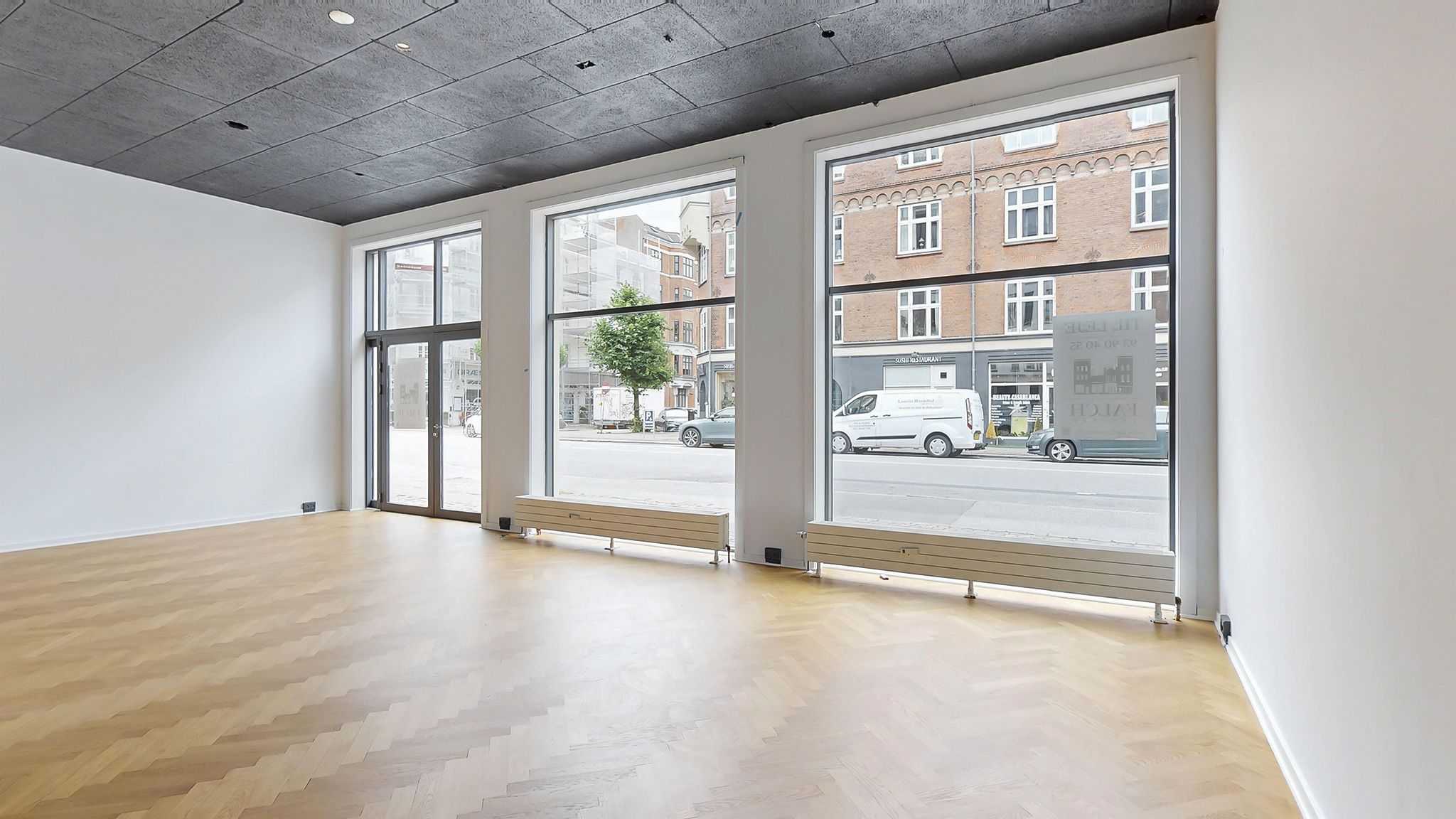 Store vinduer giver masser af dagslys til erhvervslokalet med trægulv og hvide vægge