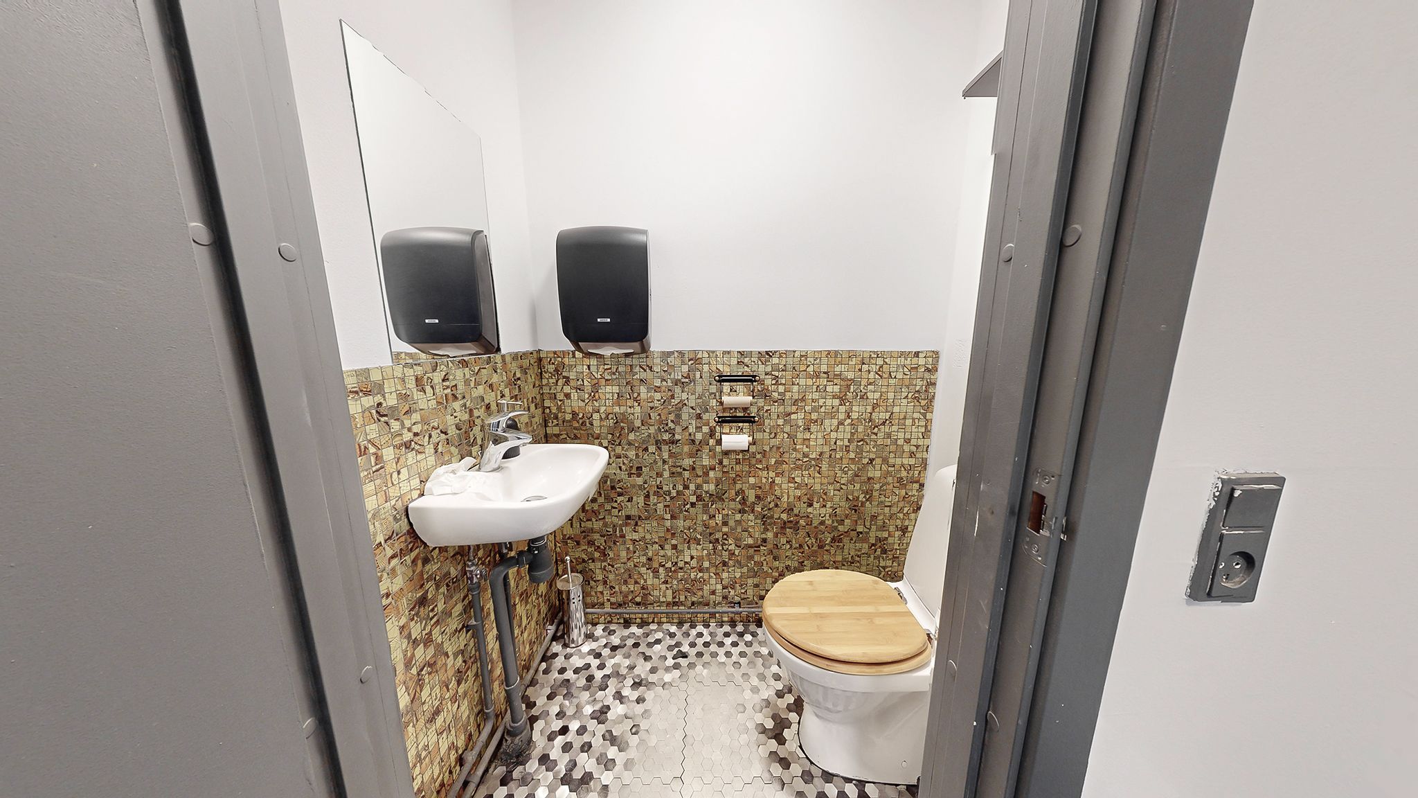 En lille toiletrum med en hvid toilet, en hvid vask og en spejl samt to håndklædeholdere